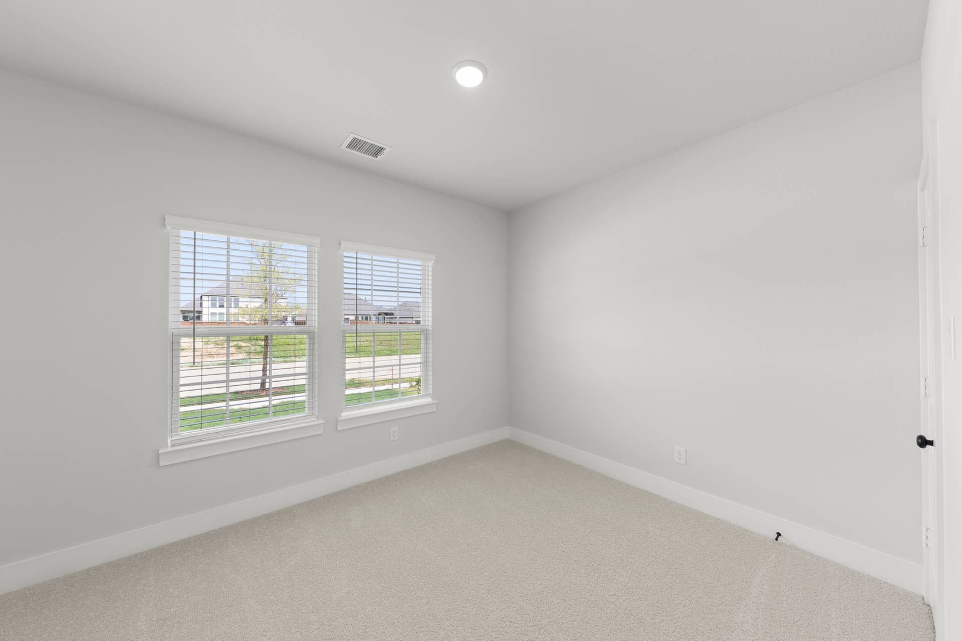 Bright bedroom with large windows and neutral carpeting.