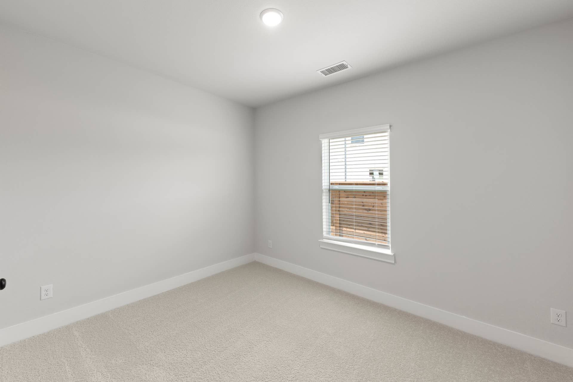 Minimalist bedroom with carpet flooring and single window with blinds.