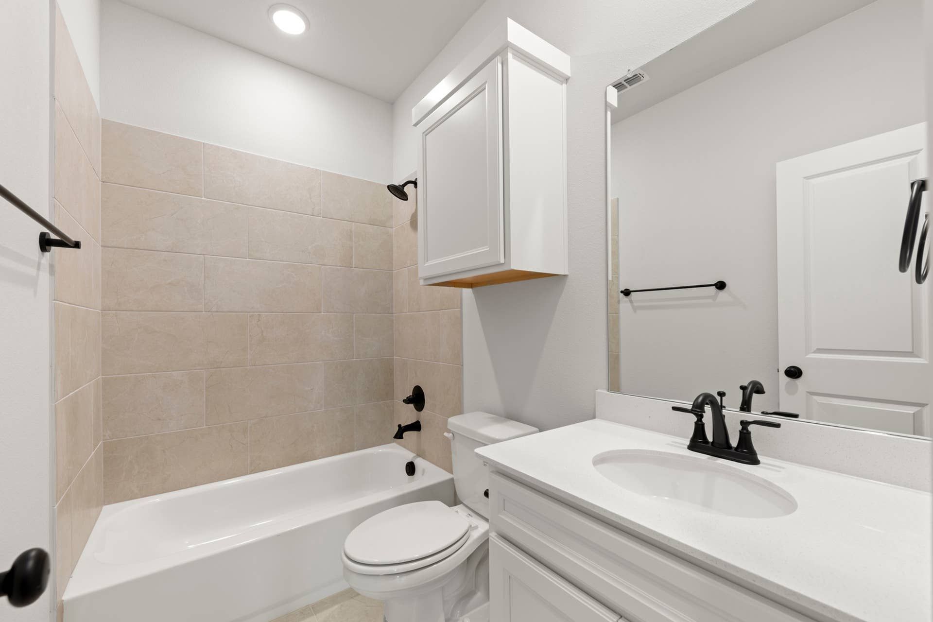 Modern bathroom with white cabinetry, beige tiled shower, and black fixtures.