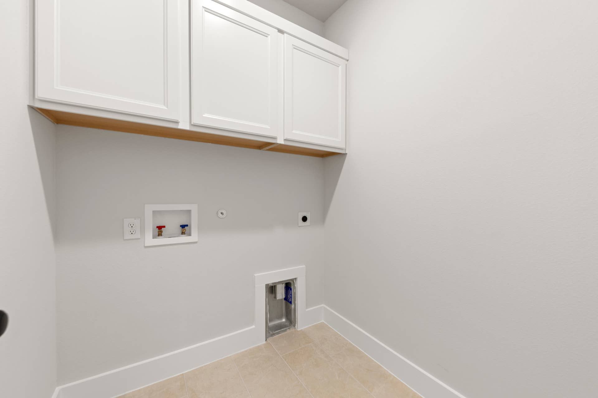 Utility room with white cabinets and laundry hookups.
