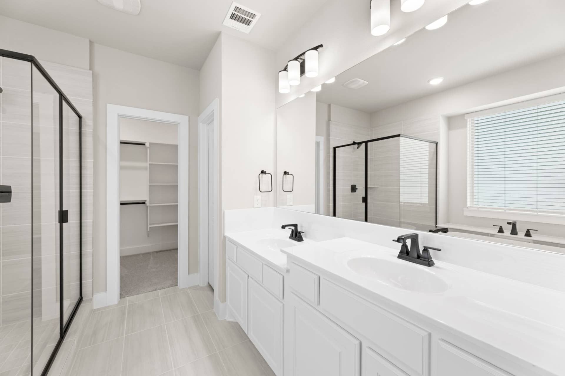 Modern bathroom with double vanity, glass shower, and walk-in closet.