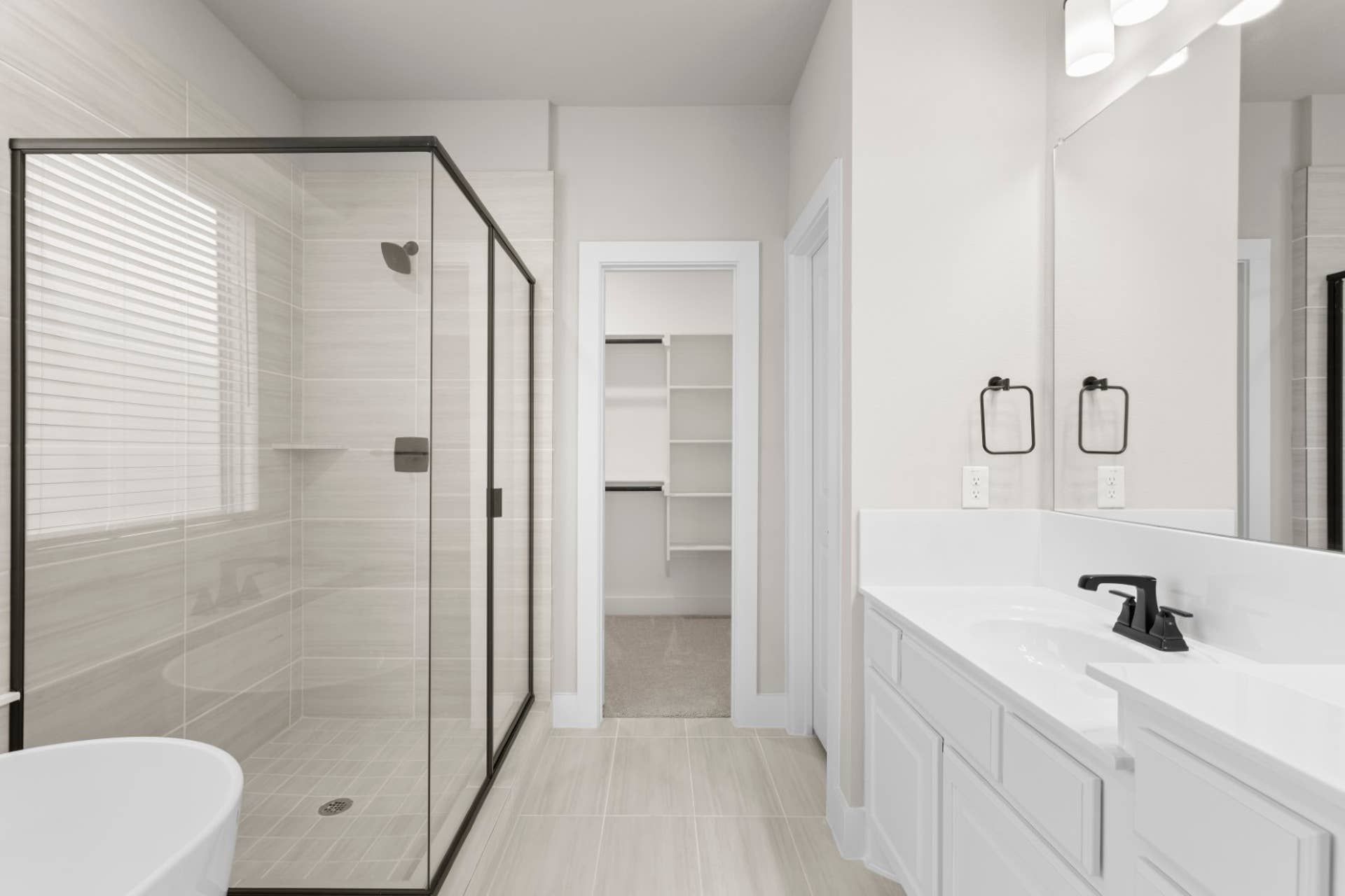 Modern bathroom with glass shower, white vanity, and walk-in closet.