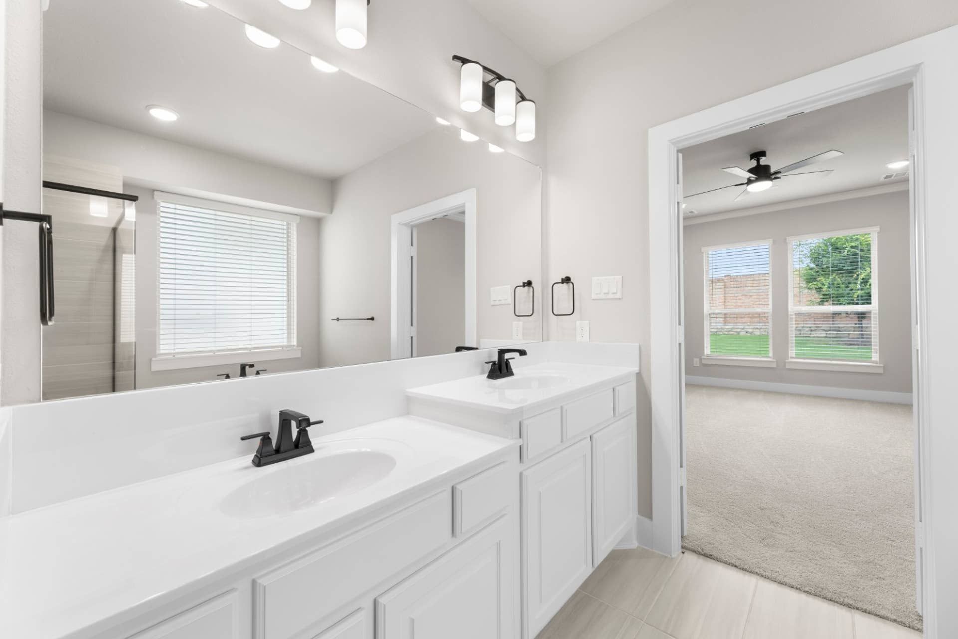 Modern bathroom with dual sinks and view into carpeted bedroom.