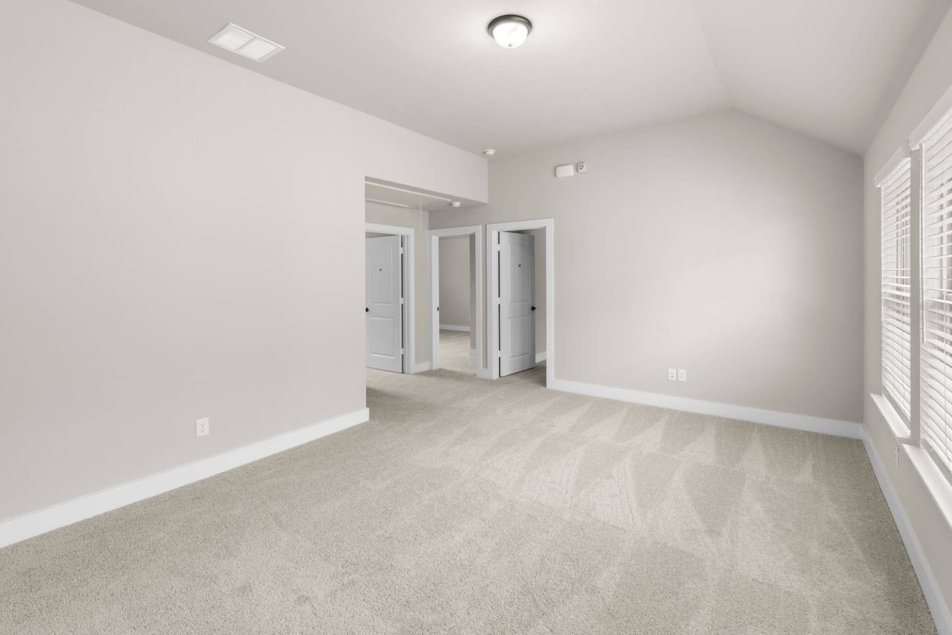 Spacious carpeted room with neutral walls and multiple doorways.