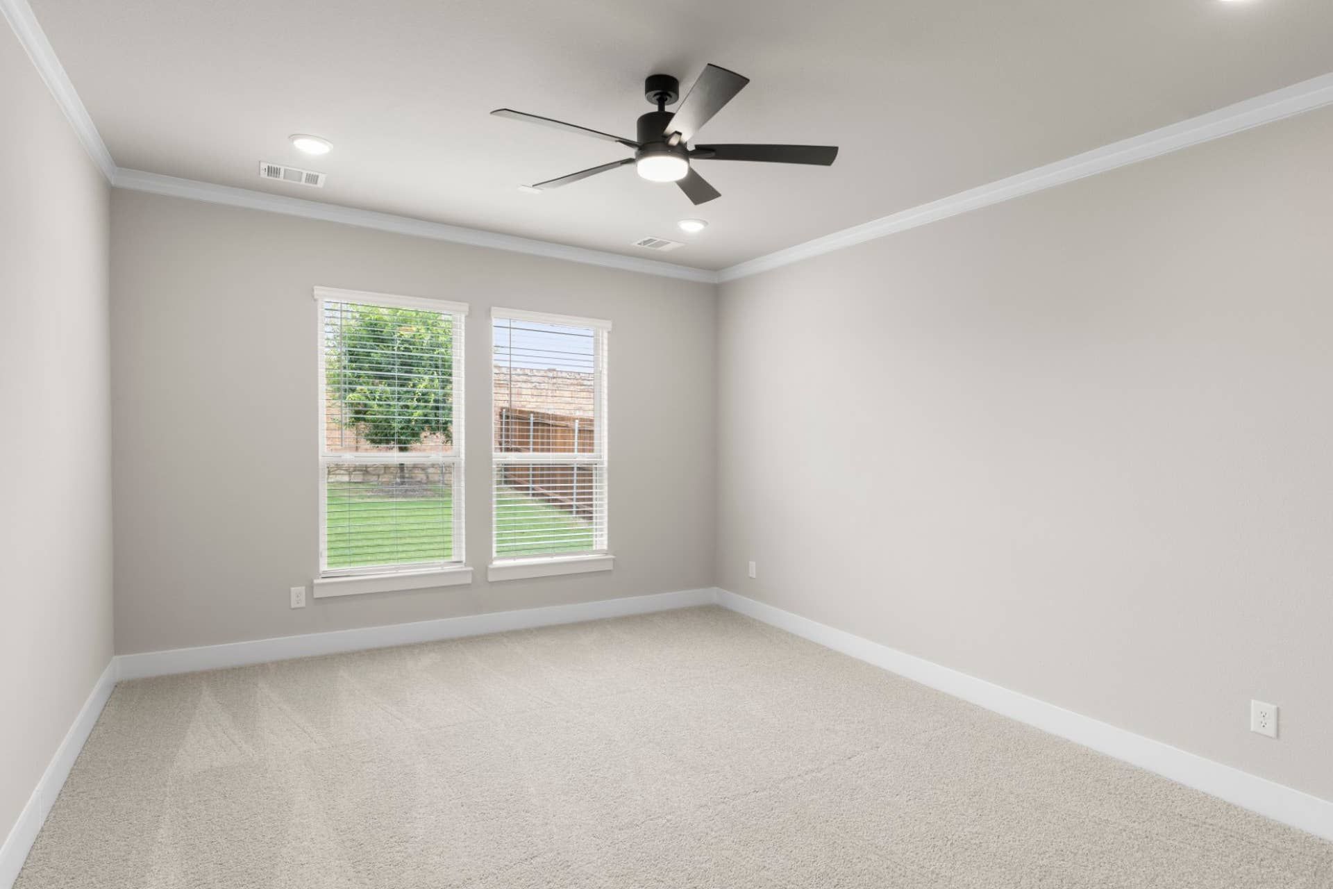 Spacious bedroom with ceiling fan and large windows overlooking backyard.