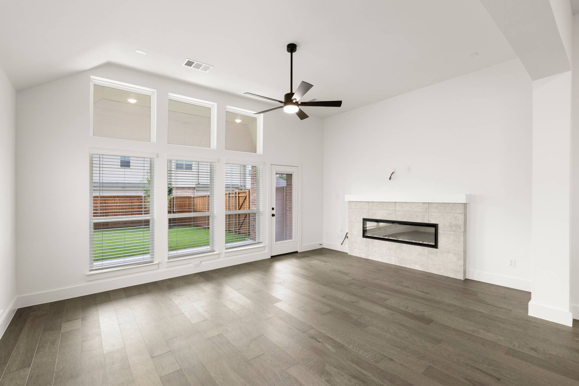 Spacious living room with large windows, modern fireplace, and ceiling fan.