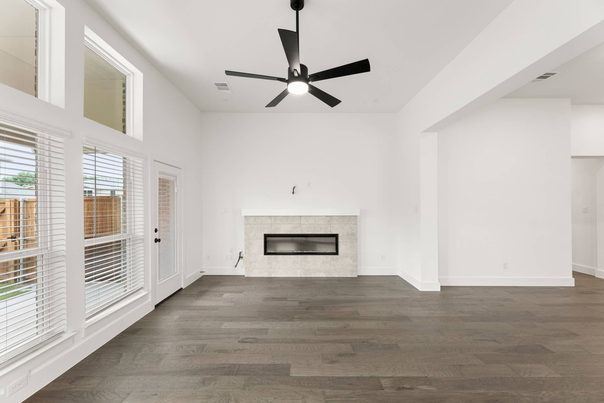 Bright modern living room with large windows, dark wood floors, and a ceiling fan.