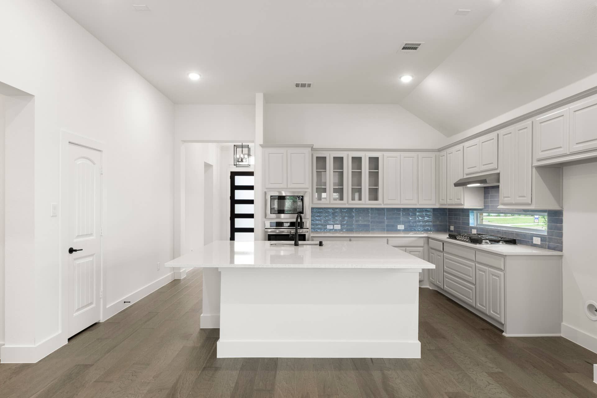 Modern kitchen with large island, white cabinetry, and blue tile backsplash.