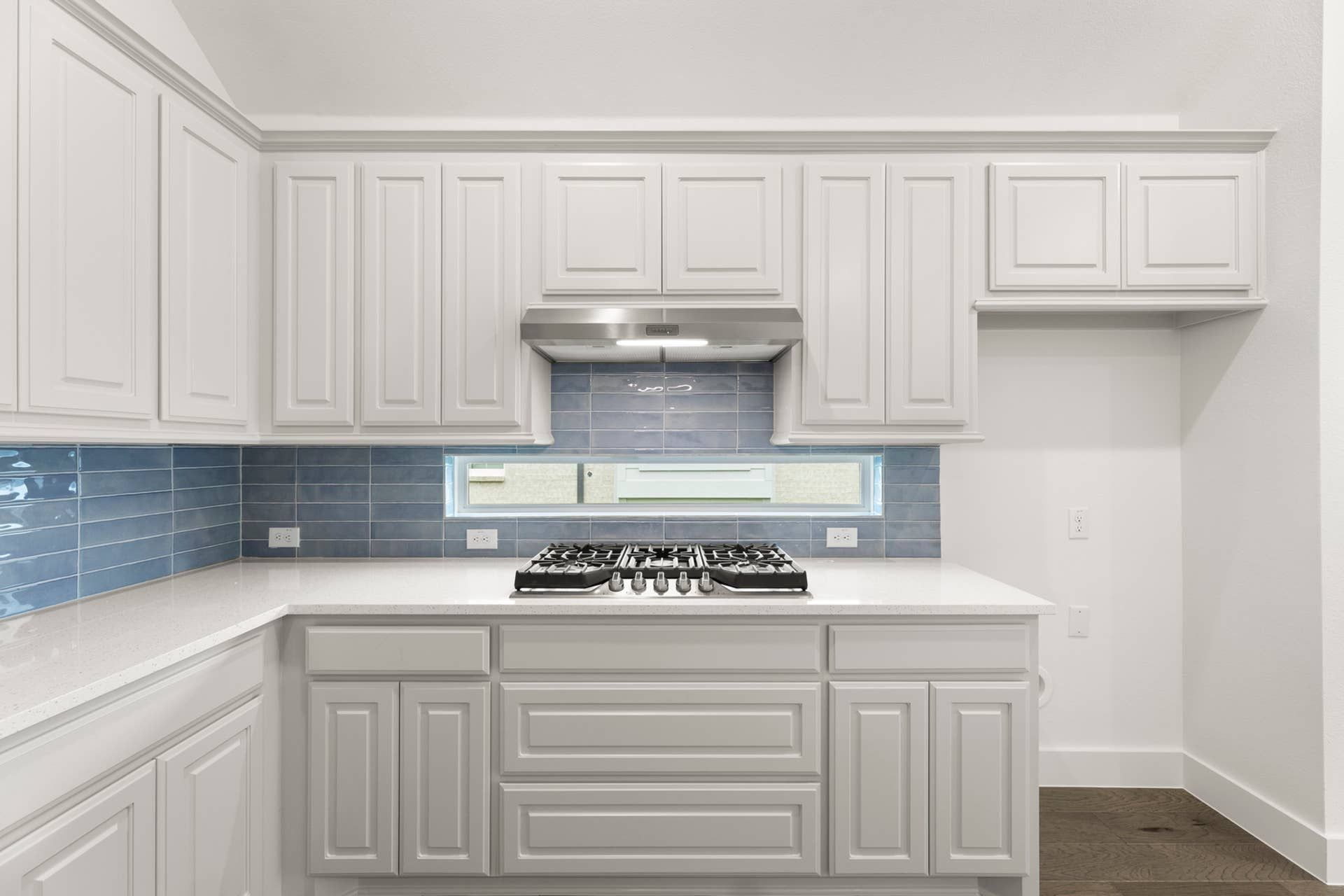 Modern kitchen with white cabinets, blue tile backsplash, and stainless steel range hood.