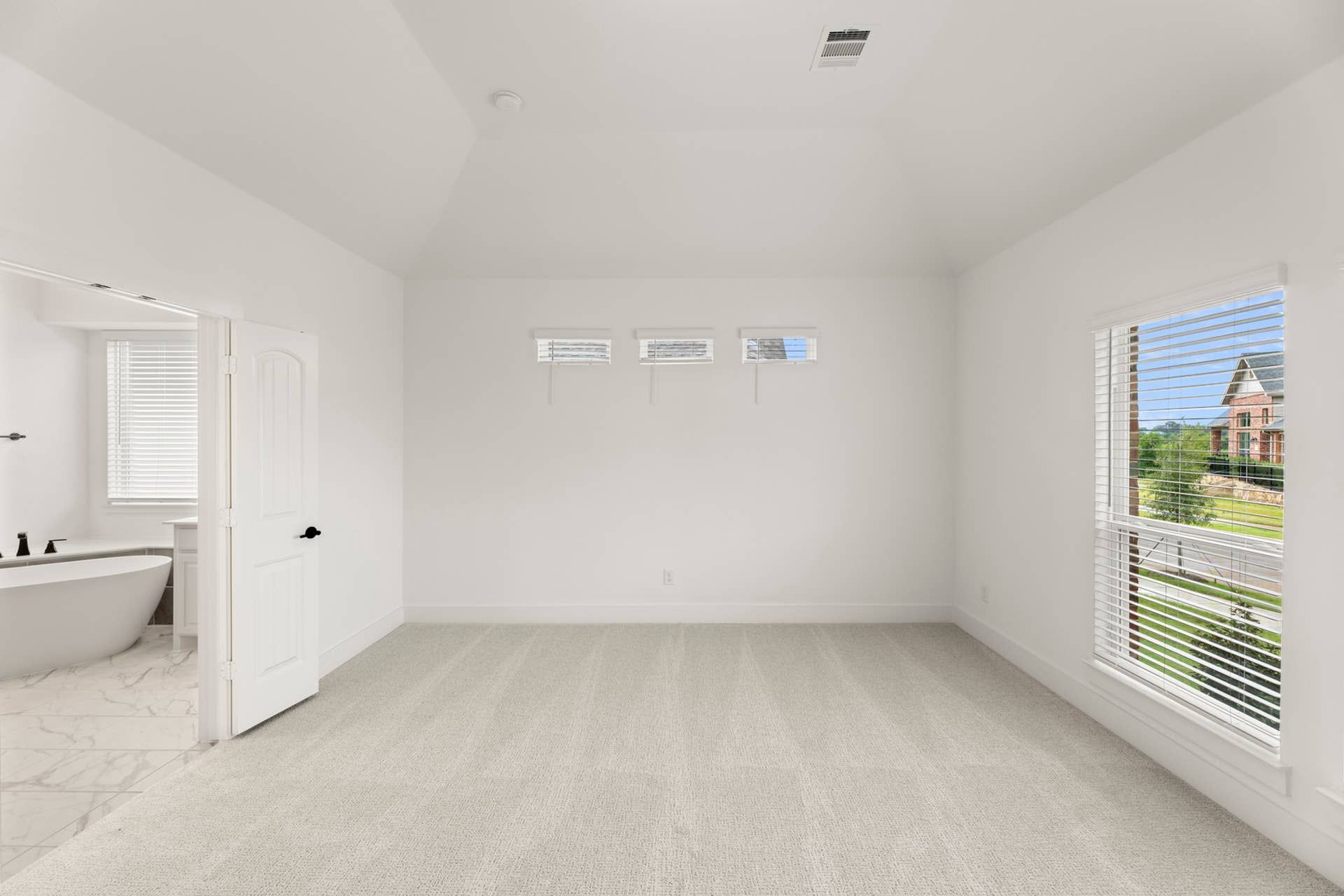Spacious bedroom with carpet flooring and adjoining bathroom with freestanding tub.