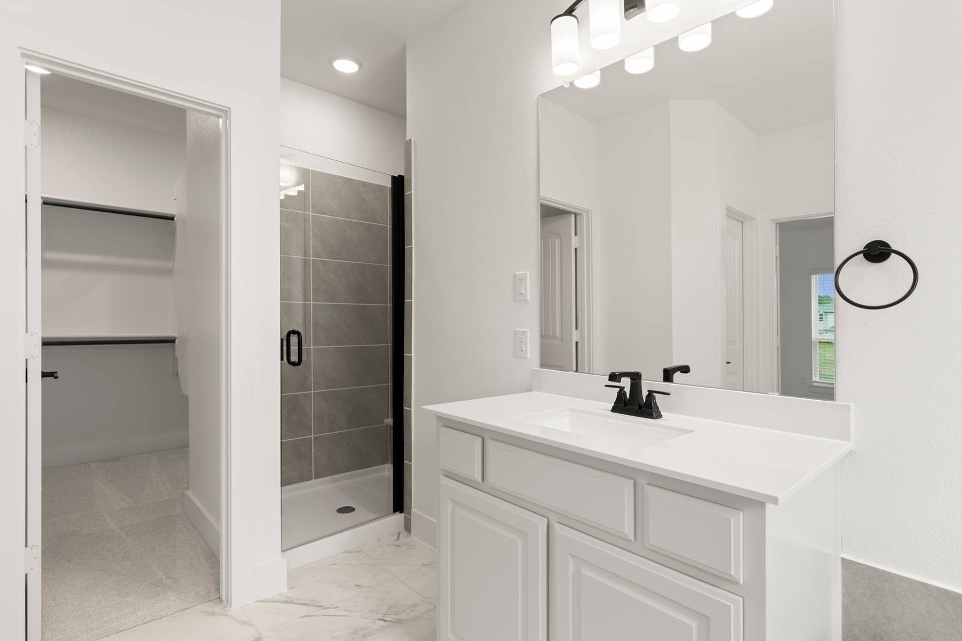 Modern bathroom with white vanity, glass shower, and walk-in closet entrance.