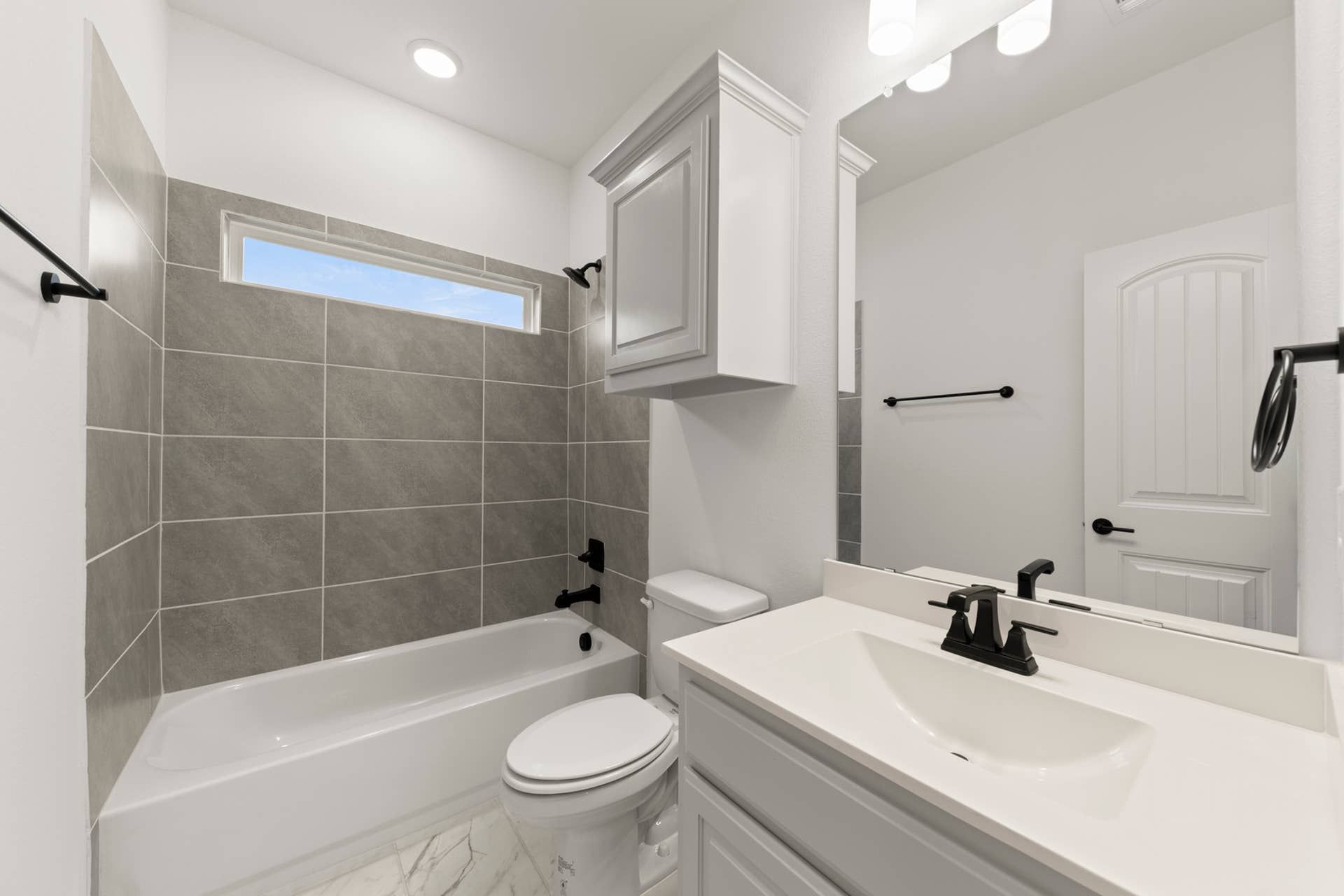 Modern bathroom with gray tiled bathtub and sleek white vanity.