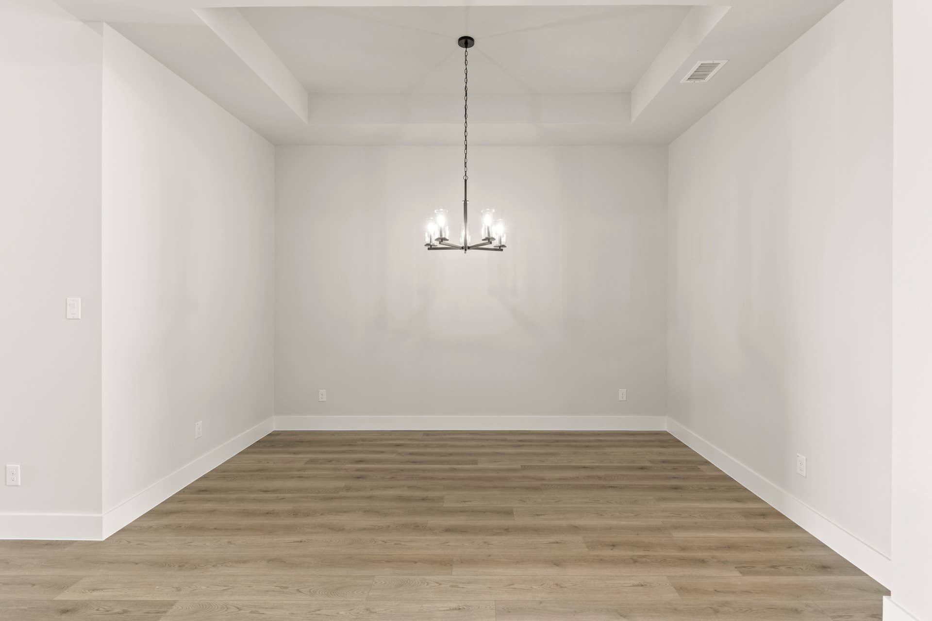 Minimalist dining room with chandelier and hardwood flooring.