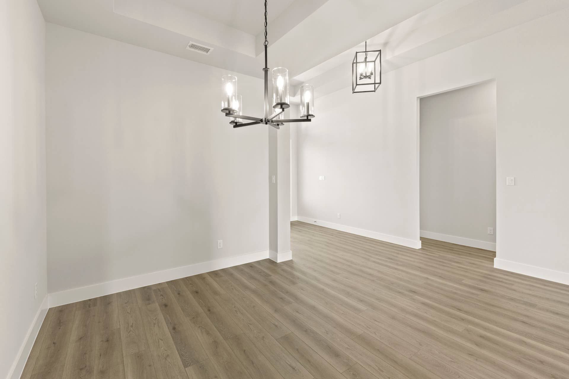Spacious dining room with modern chandelier and wood flooring.