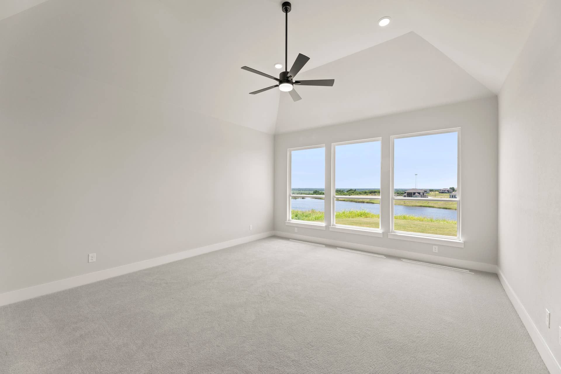 Spacious room with vaulted ceiling, large windows, and scenic water view.