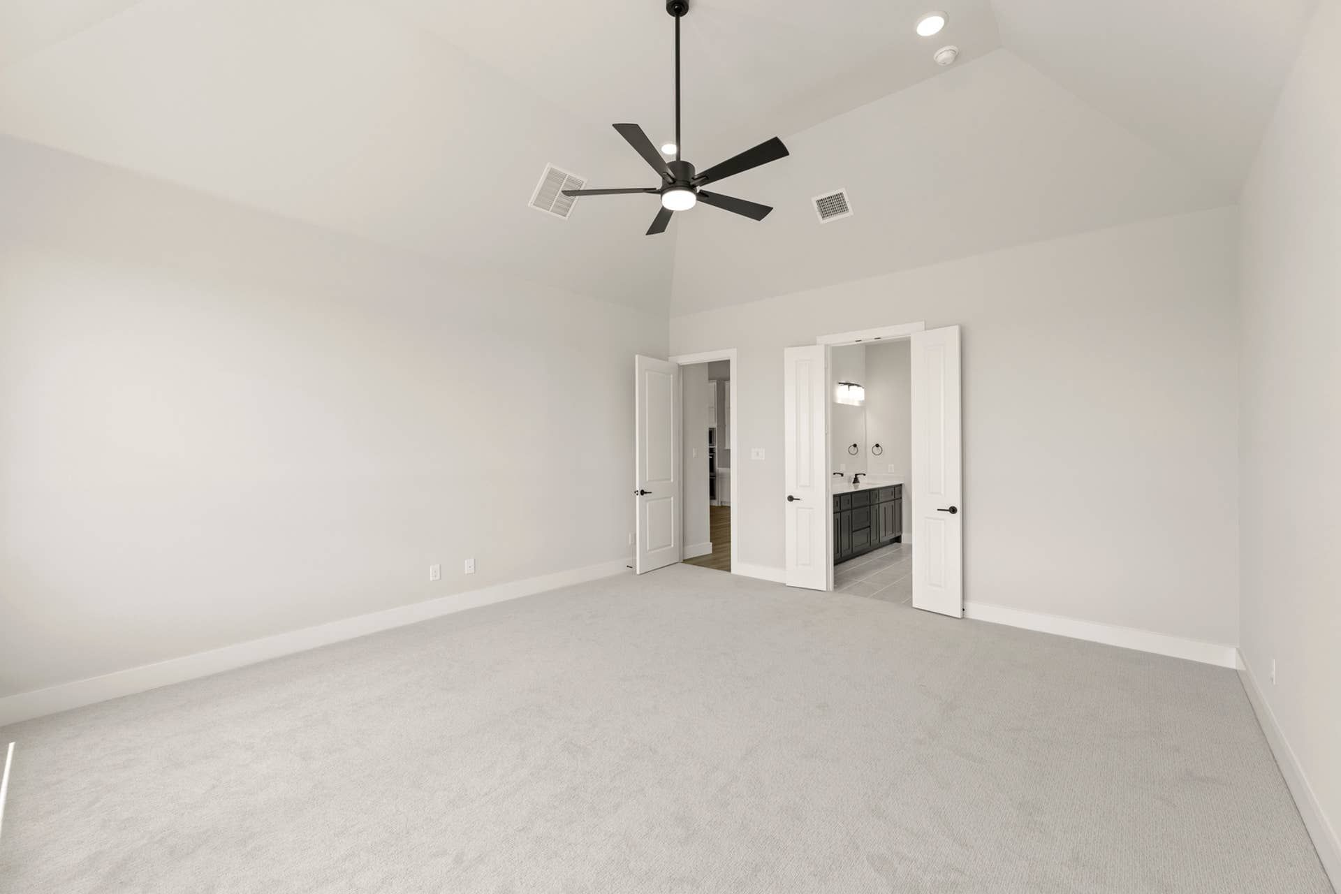 Spacious bedroom with vaulted ceiling, modern fan, and en-suite bathroom access.