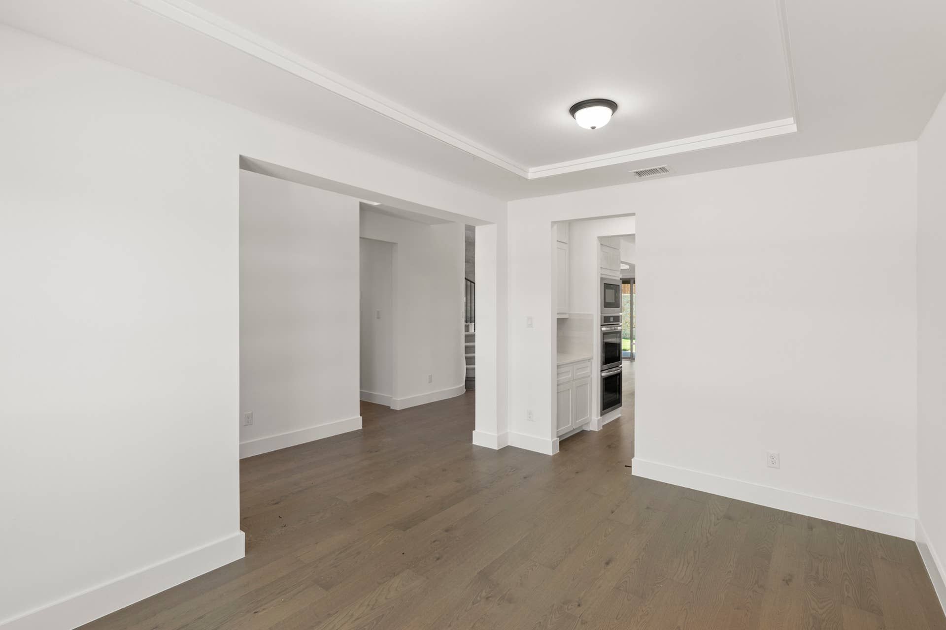 Spacious dining area with hardwood floors and white walls leading to kitchen.