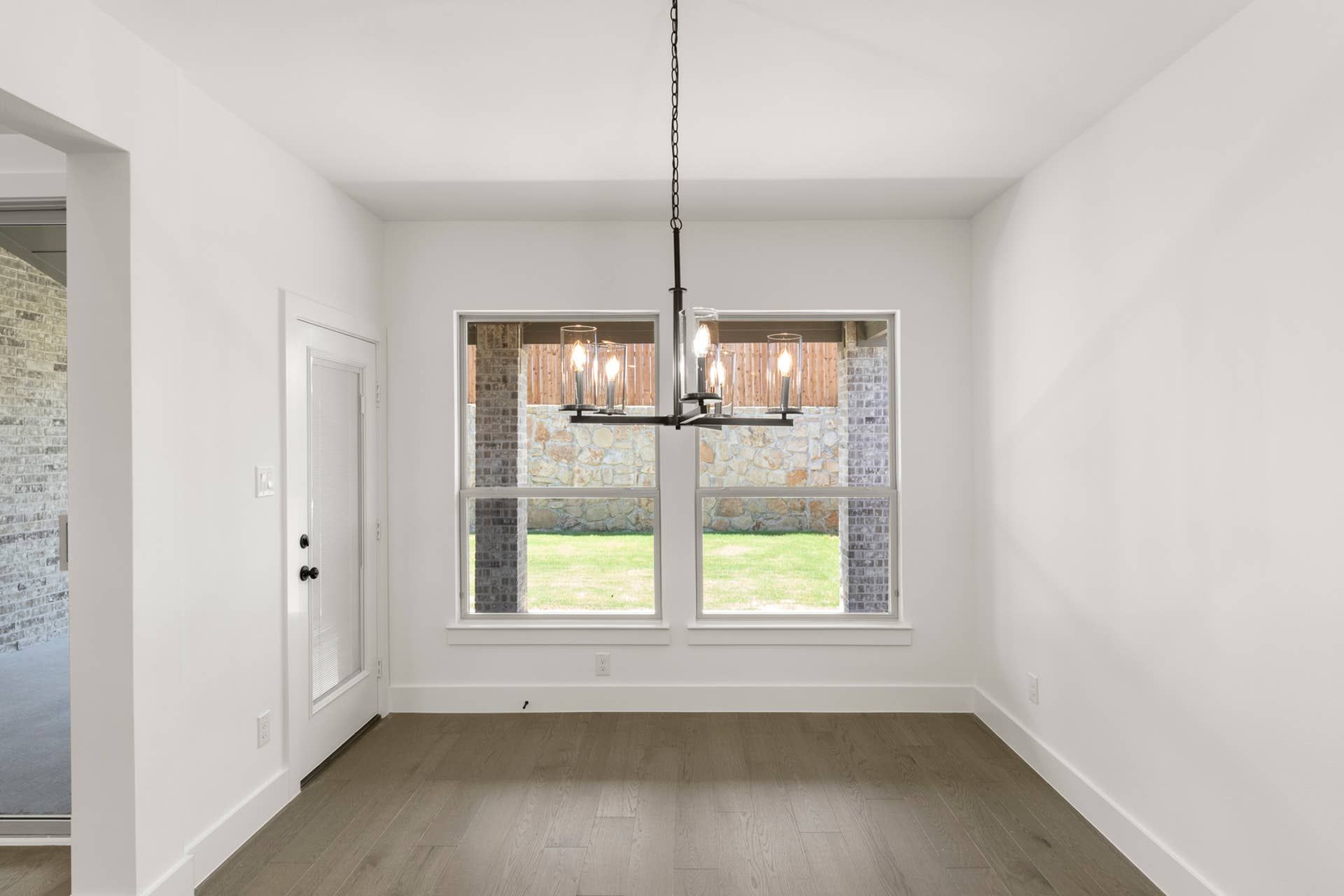 Bright dining nook with modern chandelier and large windows overlooking backyard.