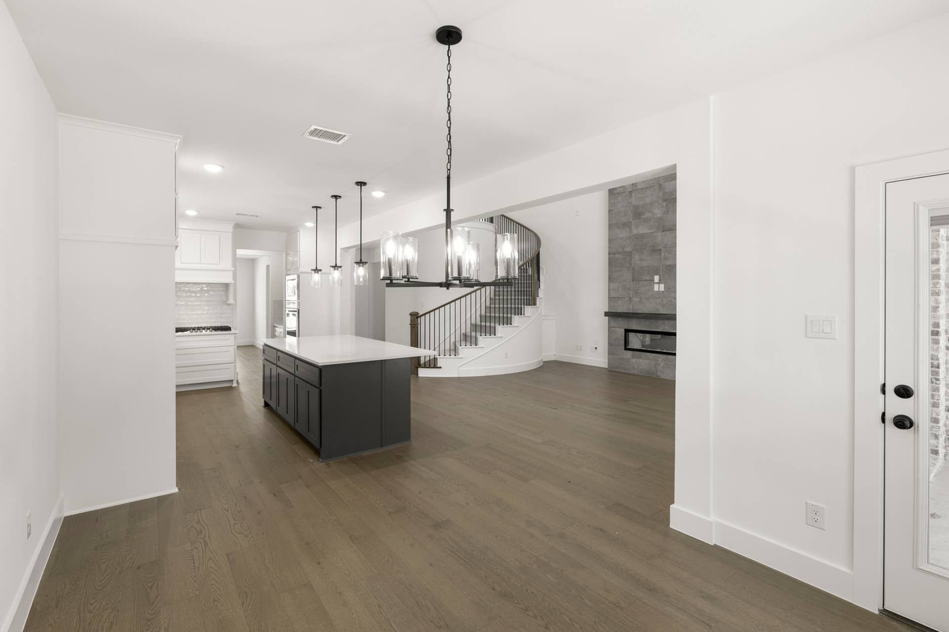 Spacious modern kitchen with island, pendant lights, and curved staircase.