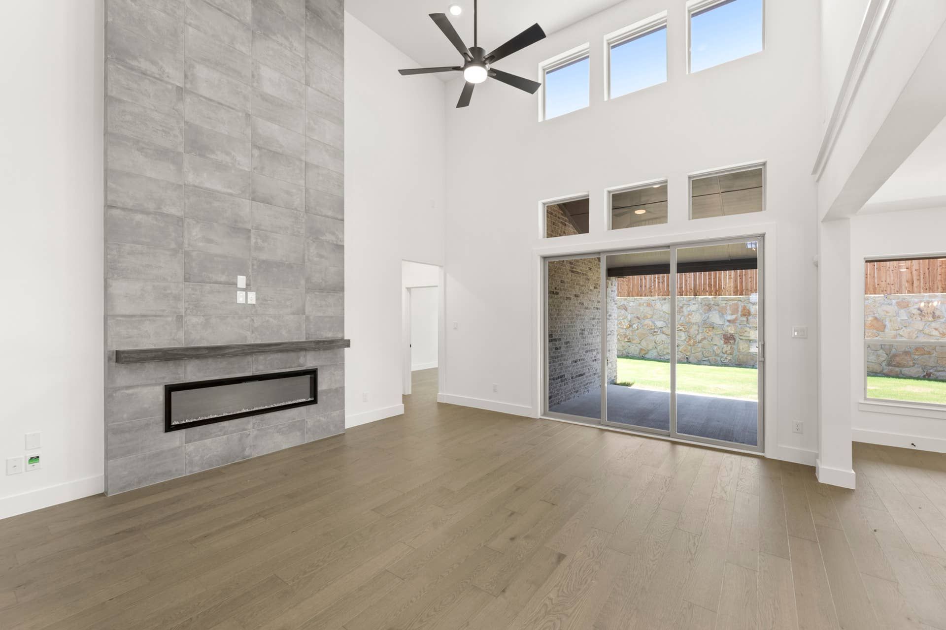 Spacious living room with high ceiling, modern fireplace, and large sliding glass doors.