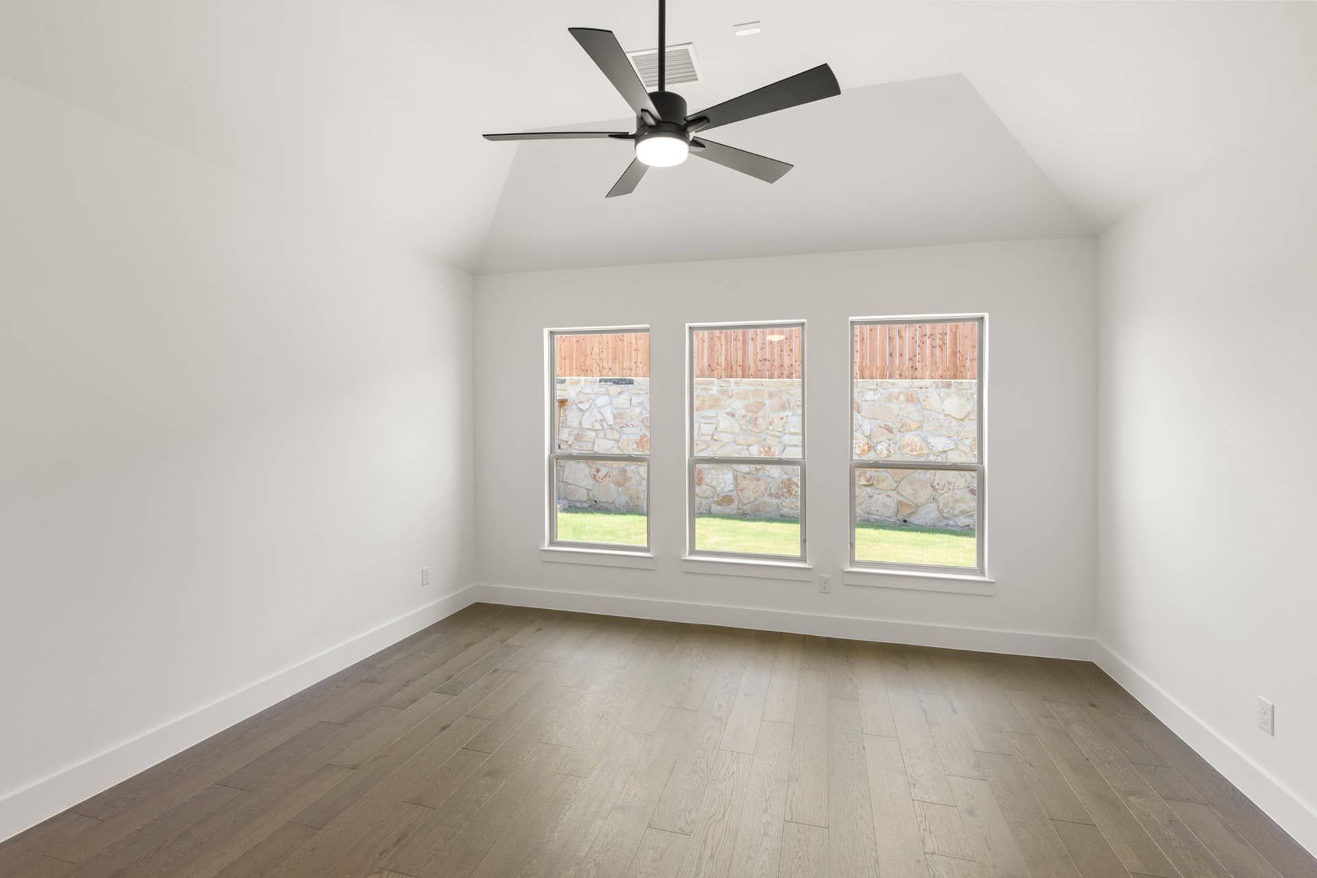 Spacious room with hardwood floor, ceiling fan, and three large windows.