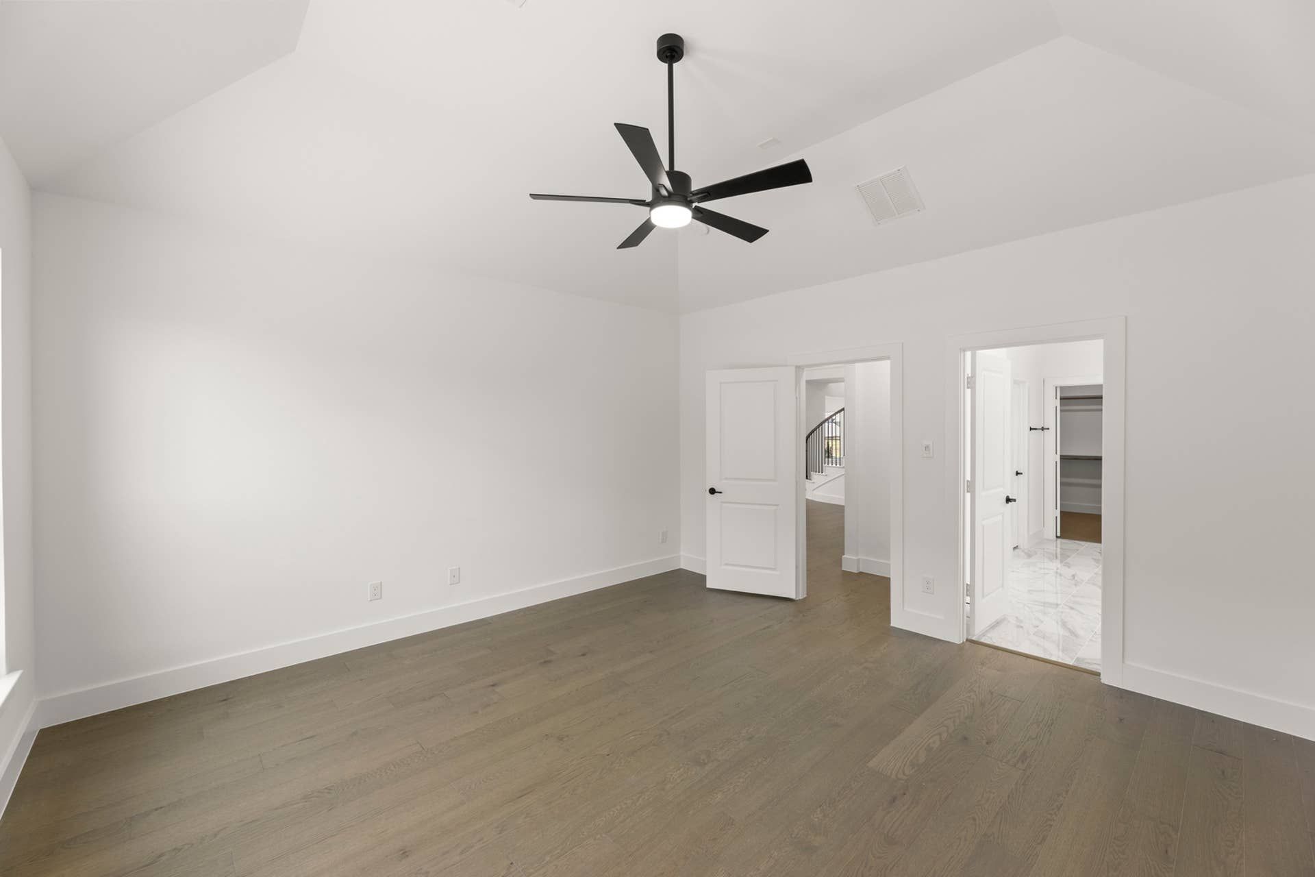 Spacious modern bedroom with wood floors, ceiling fan, and walk-in closet.