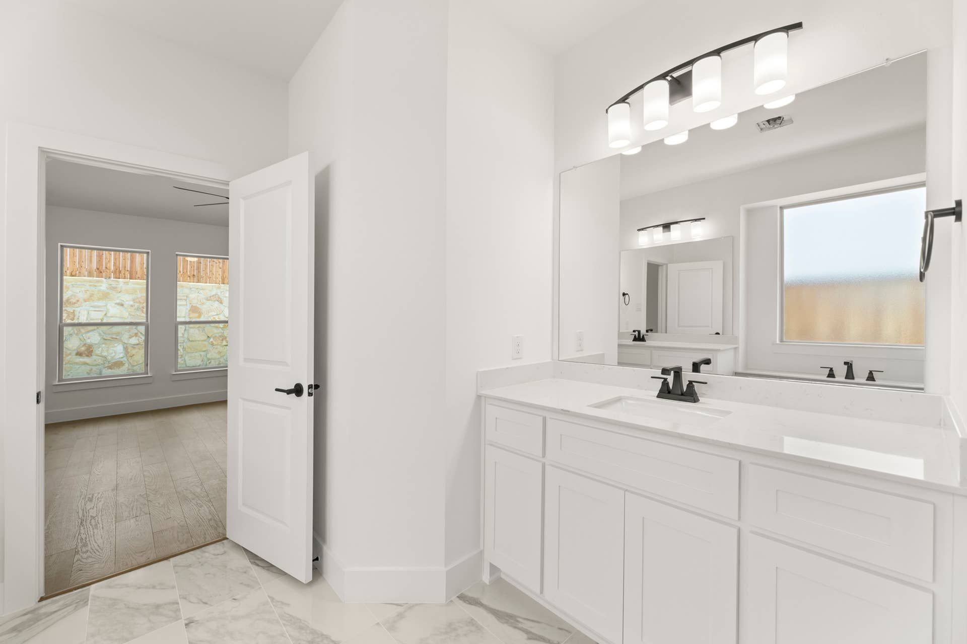 Bright bathroom with marble flooring and modern fixtures, view into adjacent room.