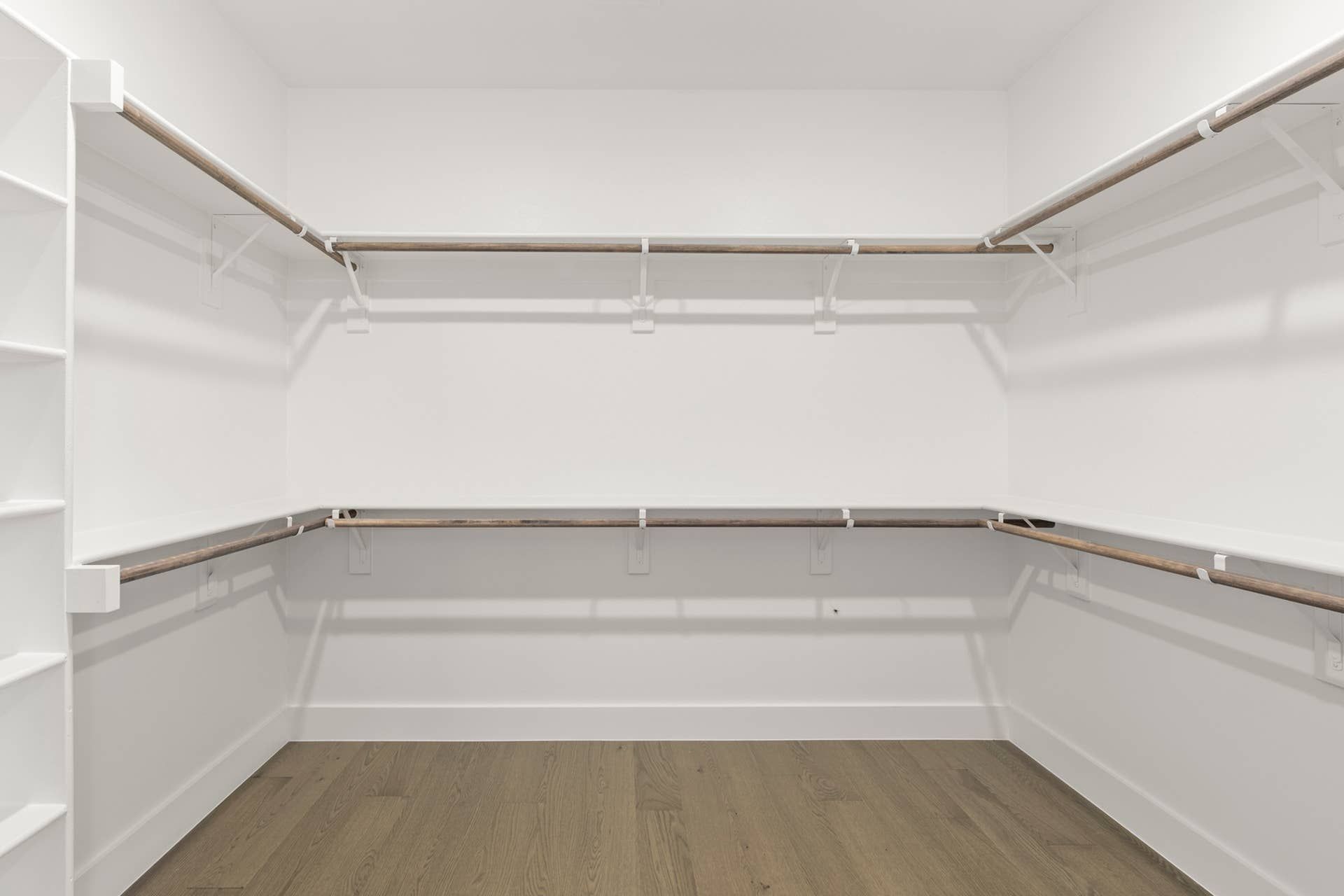 Spacious walk-in closet with wooden rods and white shelving.