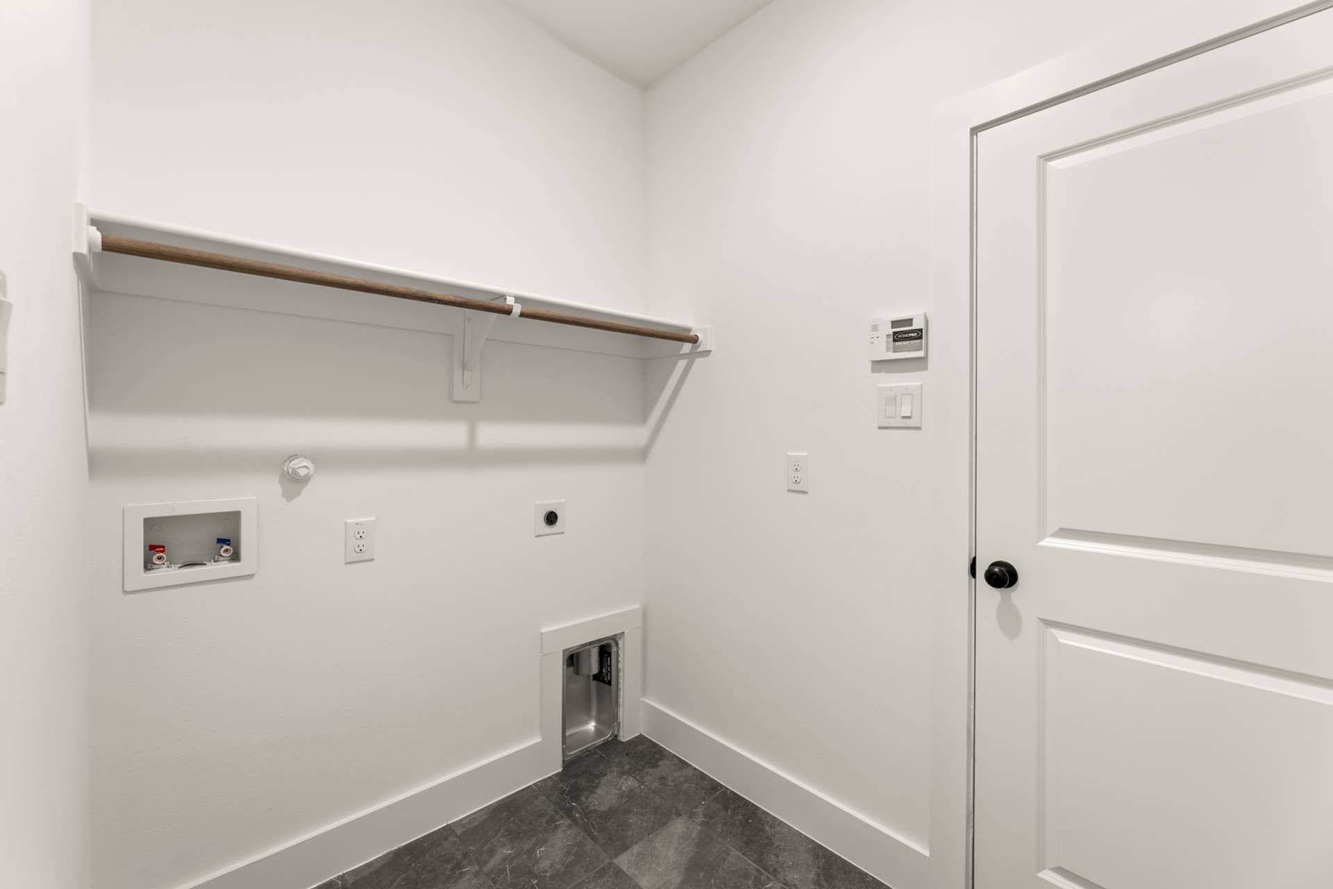 Modern utility room with plumbing hookups and white shelving.