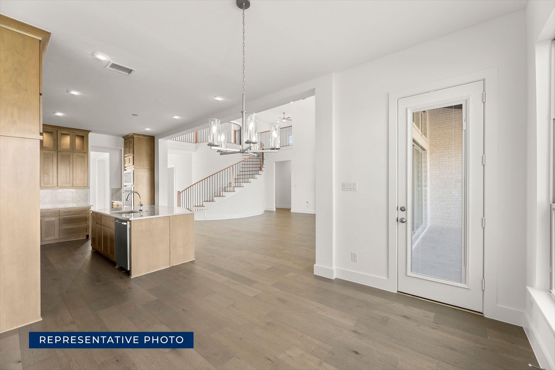 Spacious modern kitchen with island, hardwood floors, and staircase view.