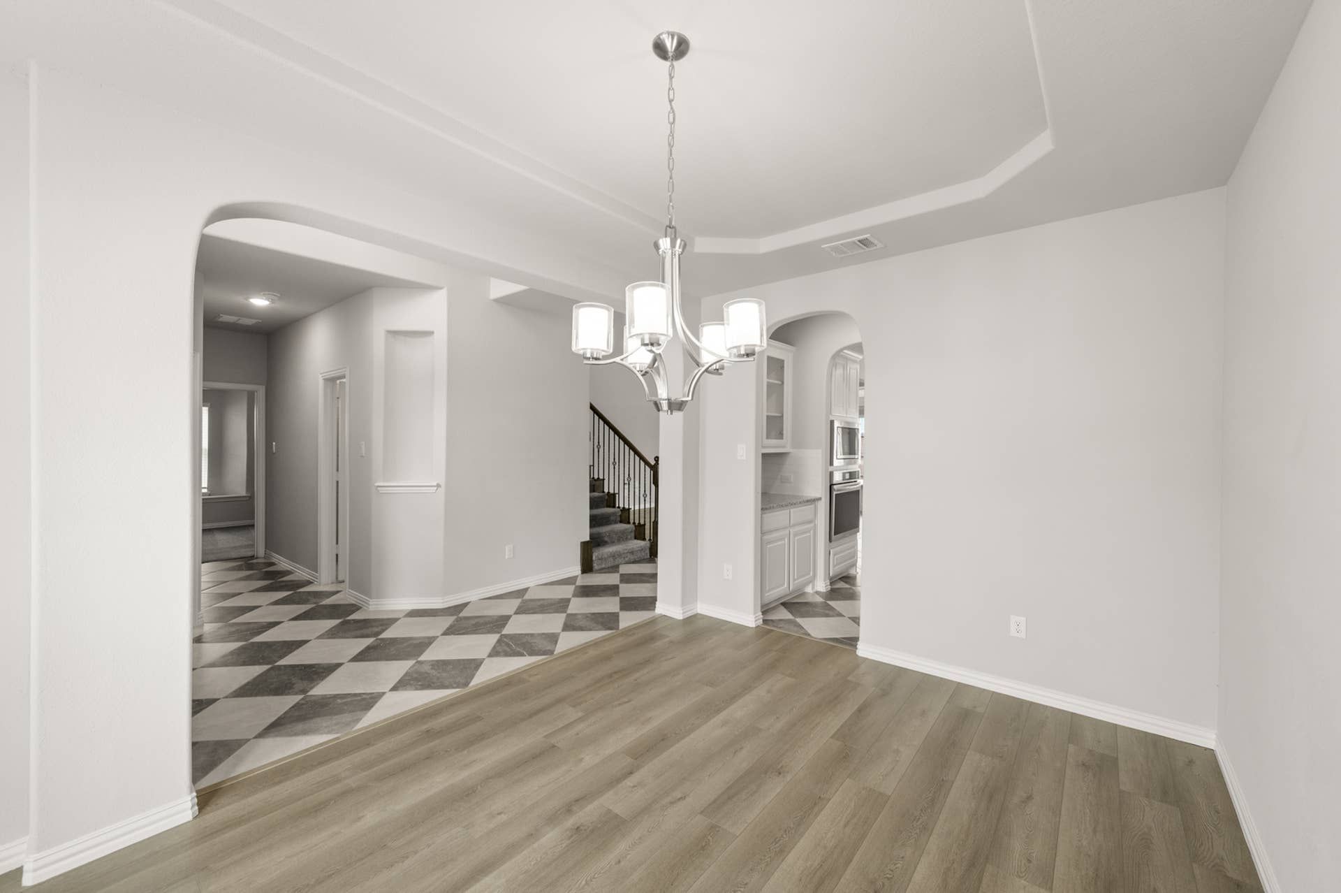 Spacious dining room with modern chandelier and arched doorway leading to kitchen.