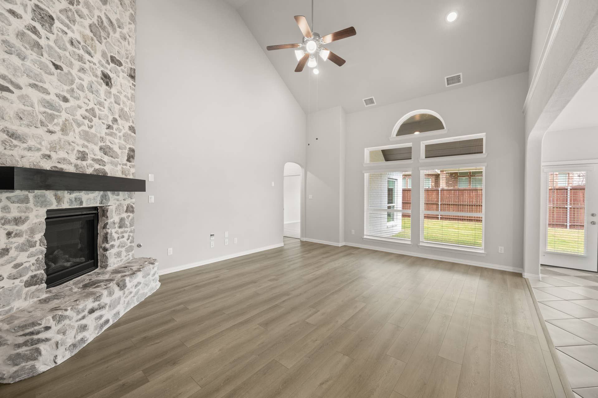 Spacious living room with stone fireplace, vaulted ceiling, and large arched windows.