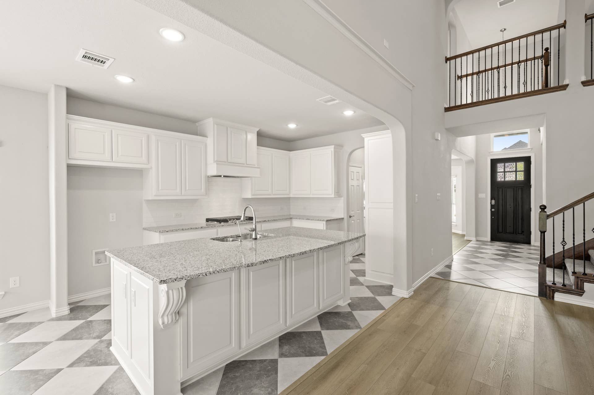 Spacious kitchen with granite island, white cabinetry, and checkered tile flooring.