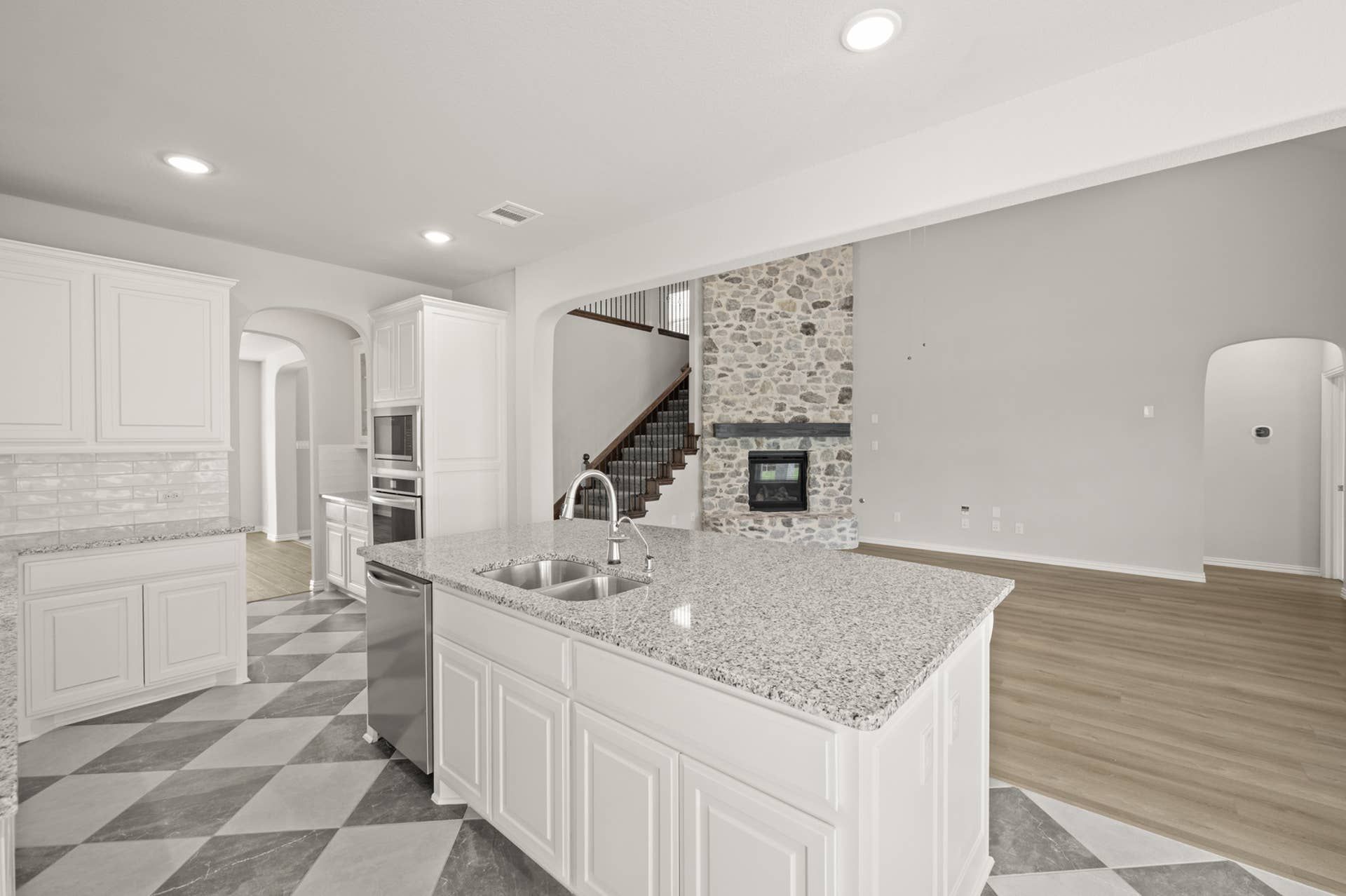 Spacious kitchen with granite countertops, stone fireplace, and checkered flooring.
