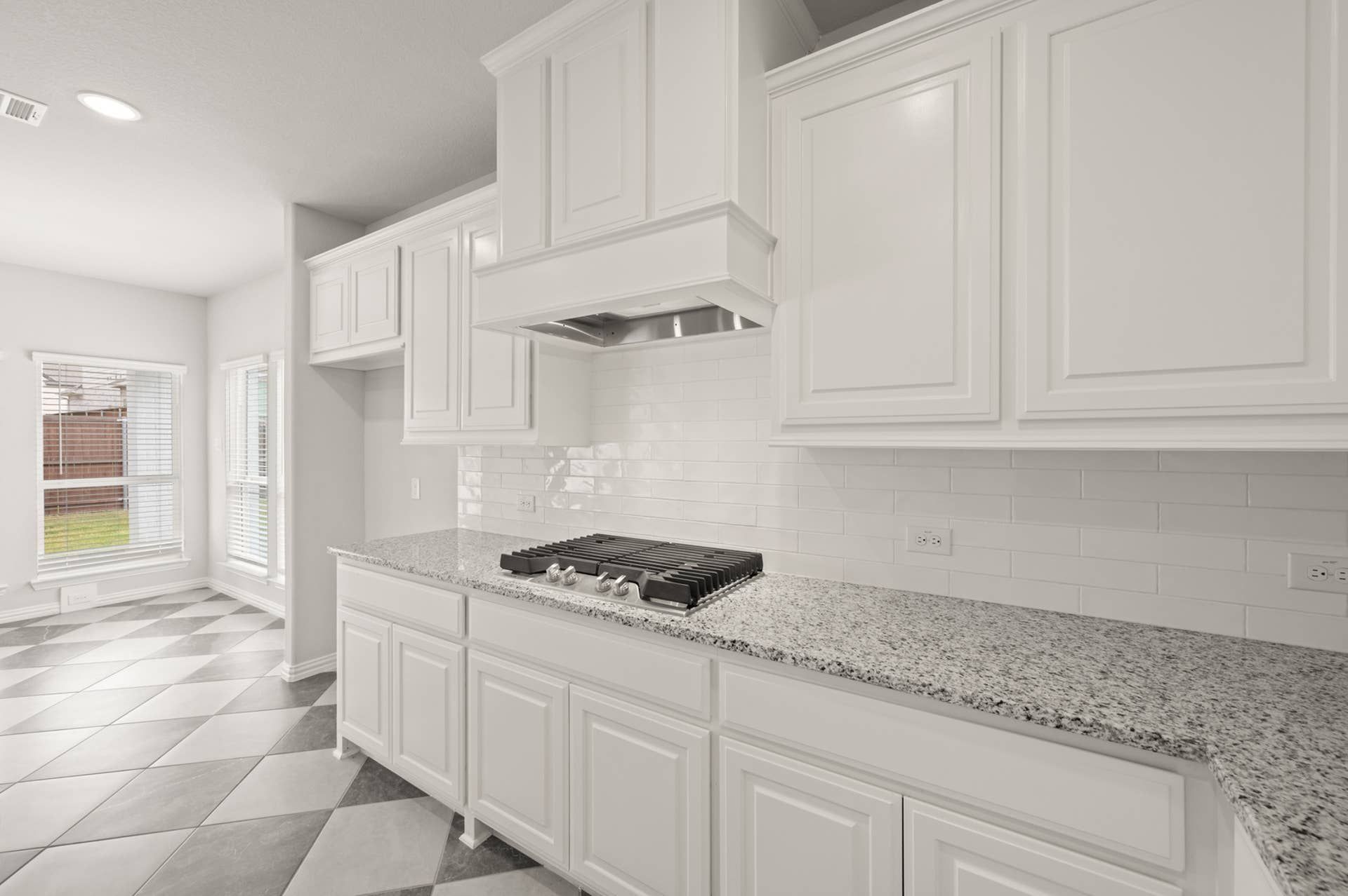 Modern kitchen with white cabinetry, granite countertops, and checkered tile flooring.