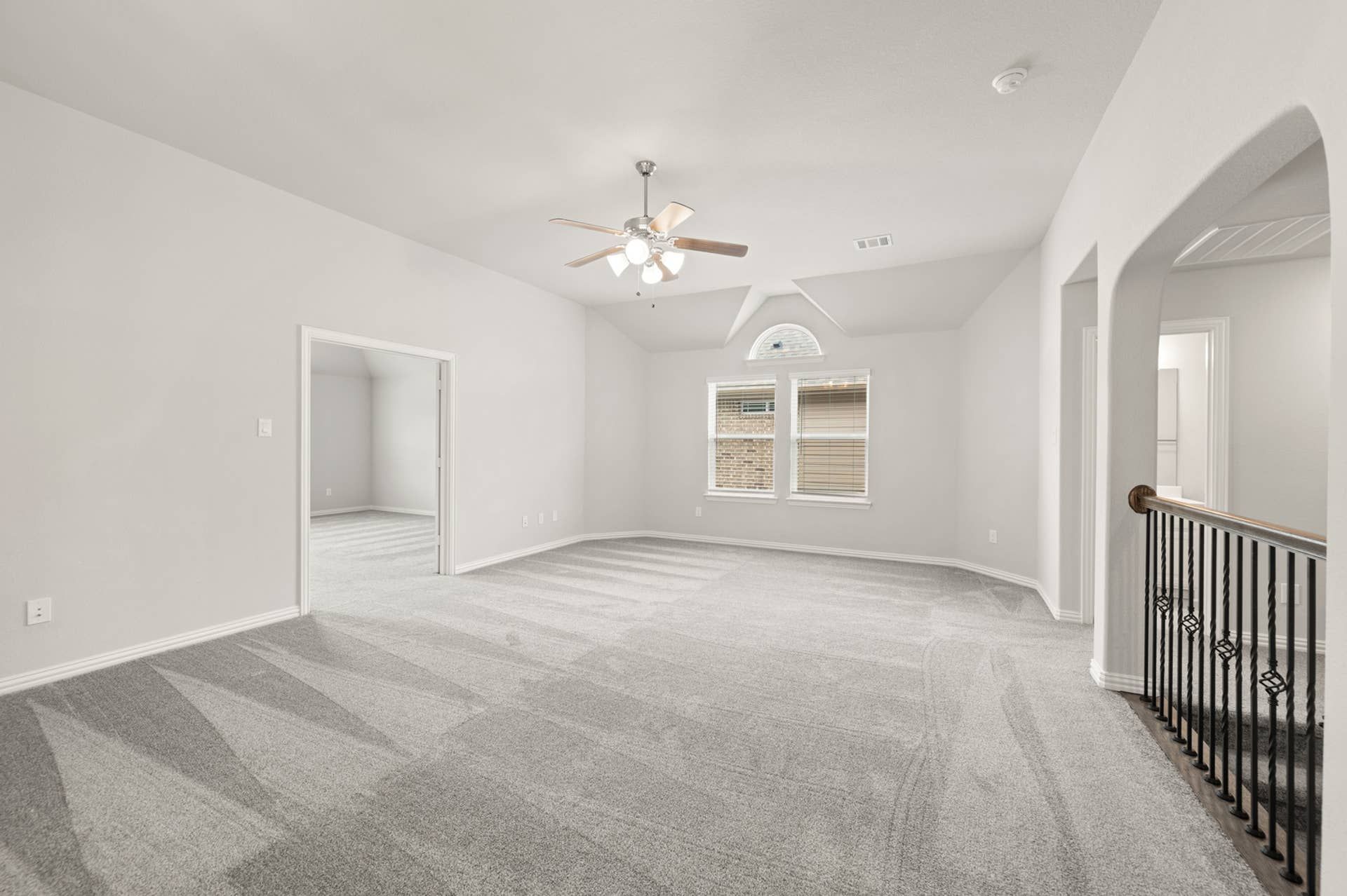 Spacious loft with vaulted ceiling, neutral carpet, and ceiling fan.
