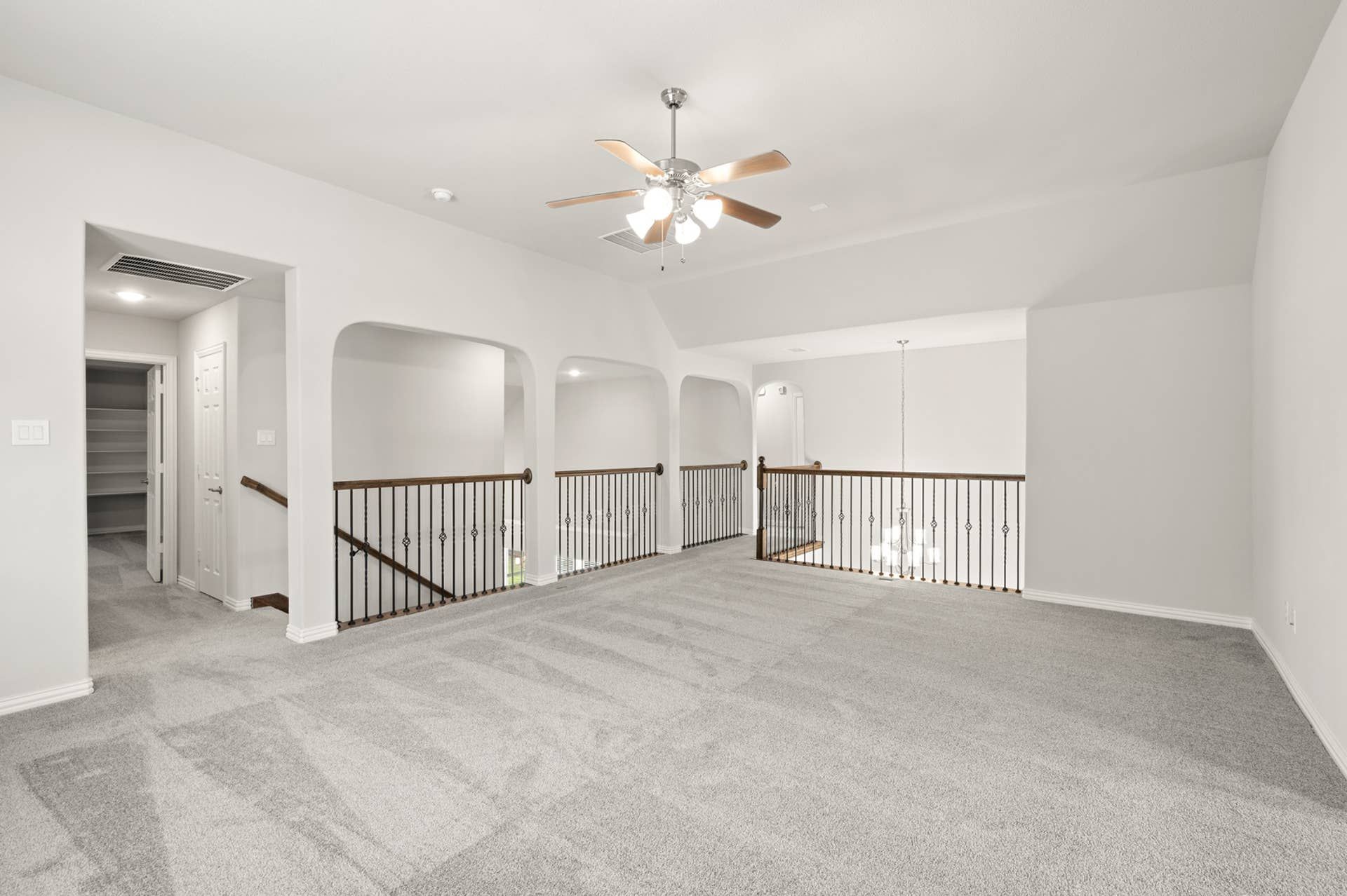 Spacious loft with carpet flooring, ceiling fan, and decorative railing.