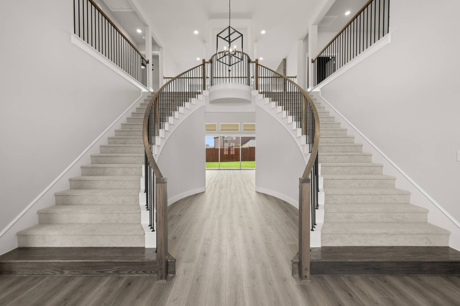 Grand double staircase with wooden railings and elegant chandelier in entryway.