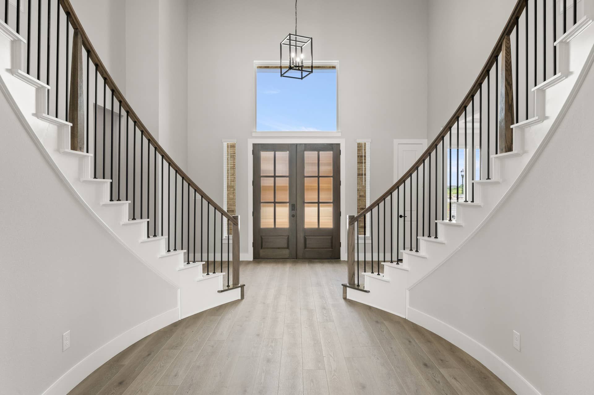Elegant double staircase entryway with modern chandelier and wooden floors.