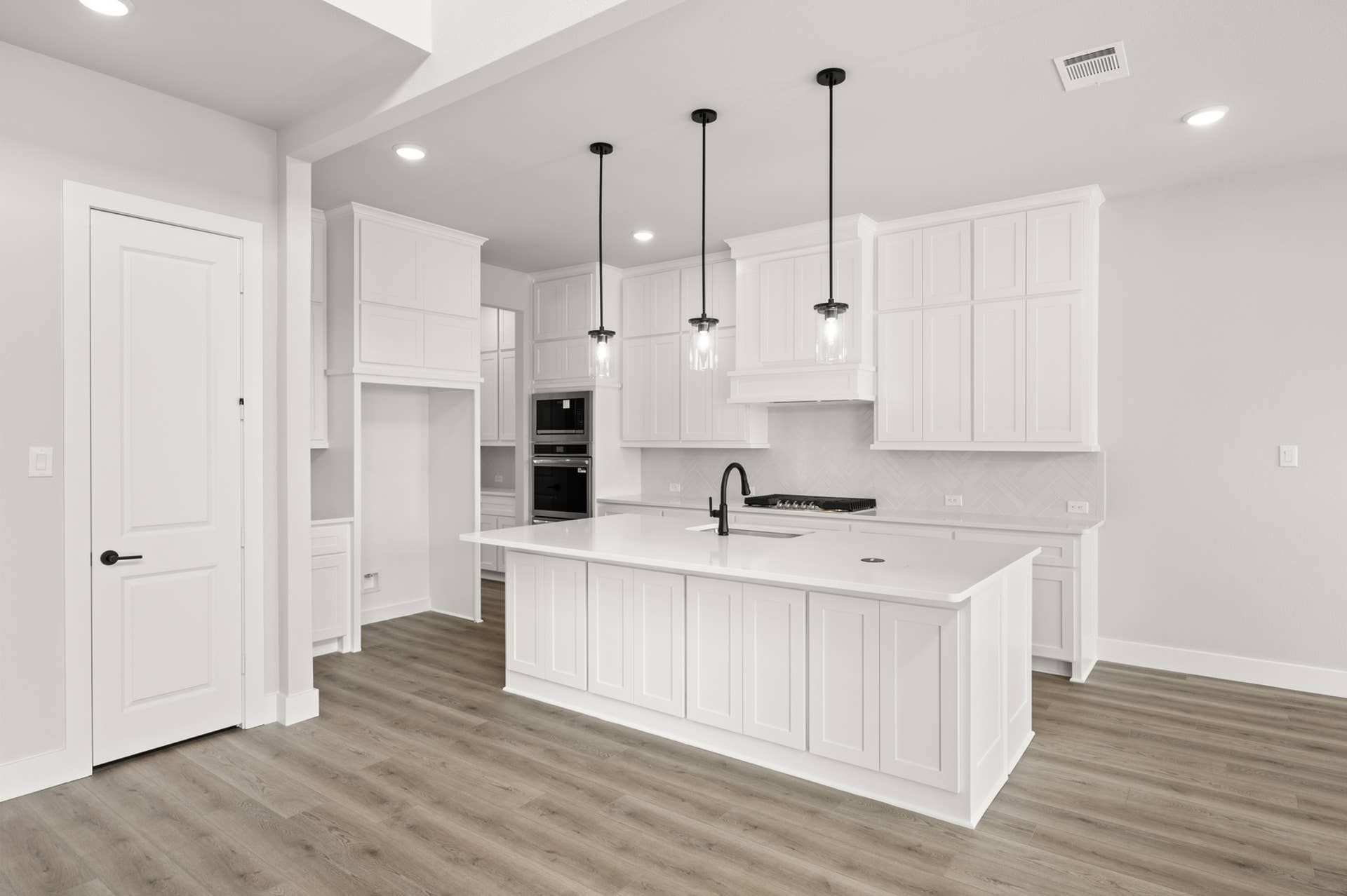 Modern white kitchen with island, pendant lighting, and hardwood floors.