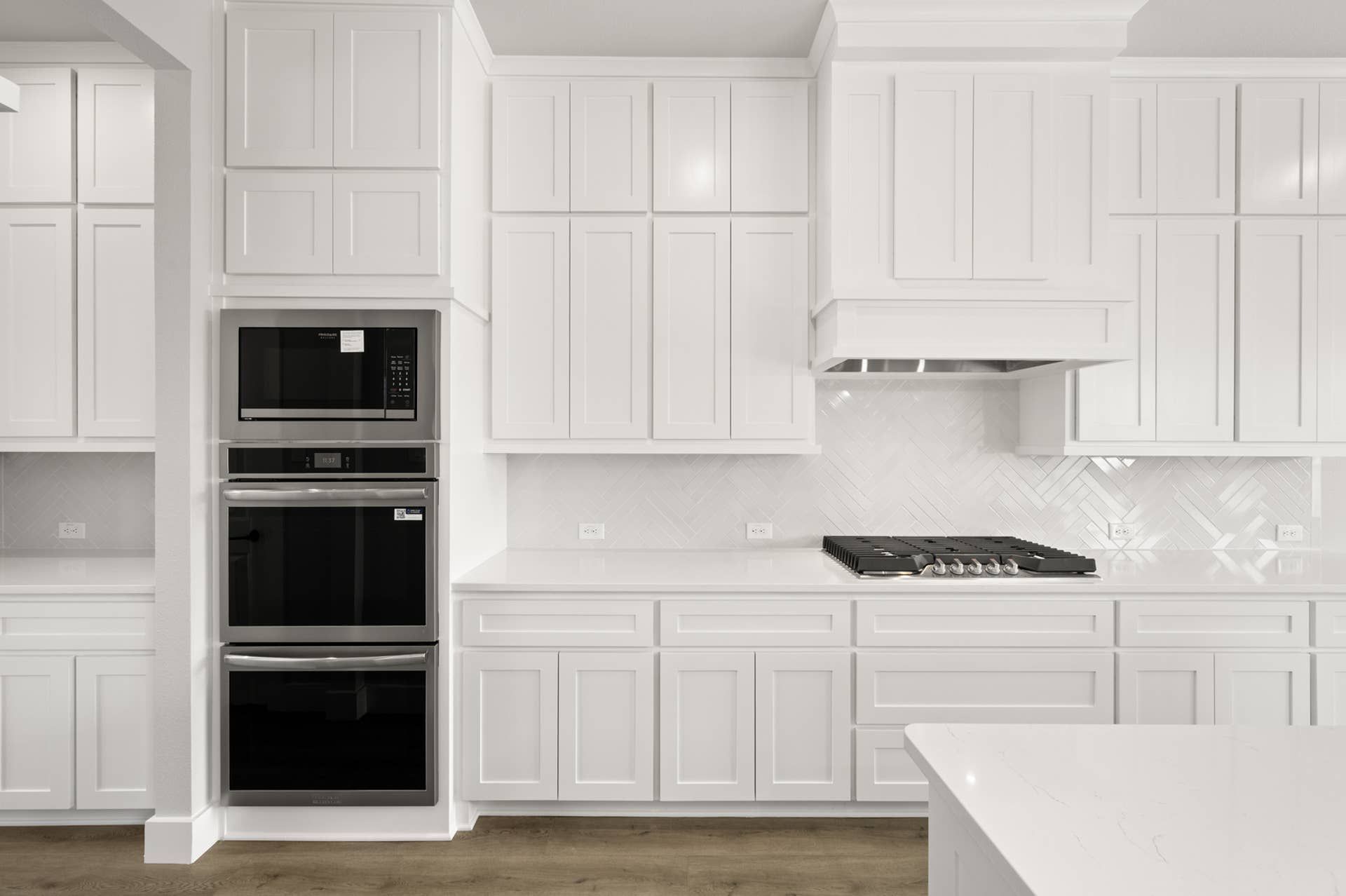 Modern kitchen with white cabinetry, stainless steel appliances, and herringbone backsplash.
