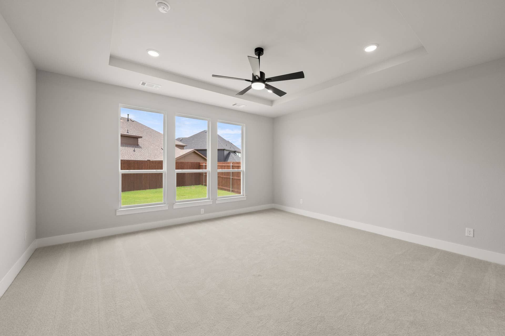 Spacious primary suite with large windows and ceiling fan.