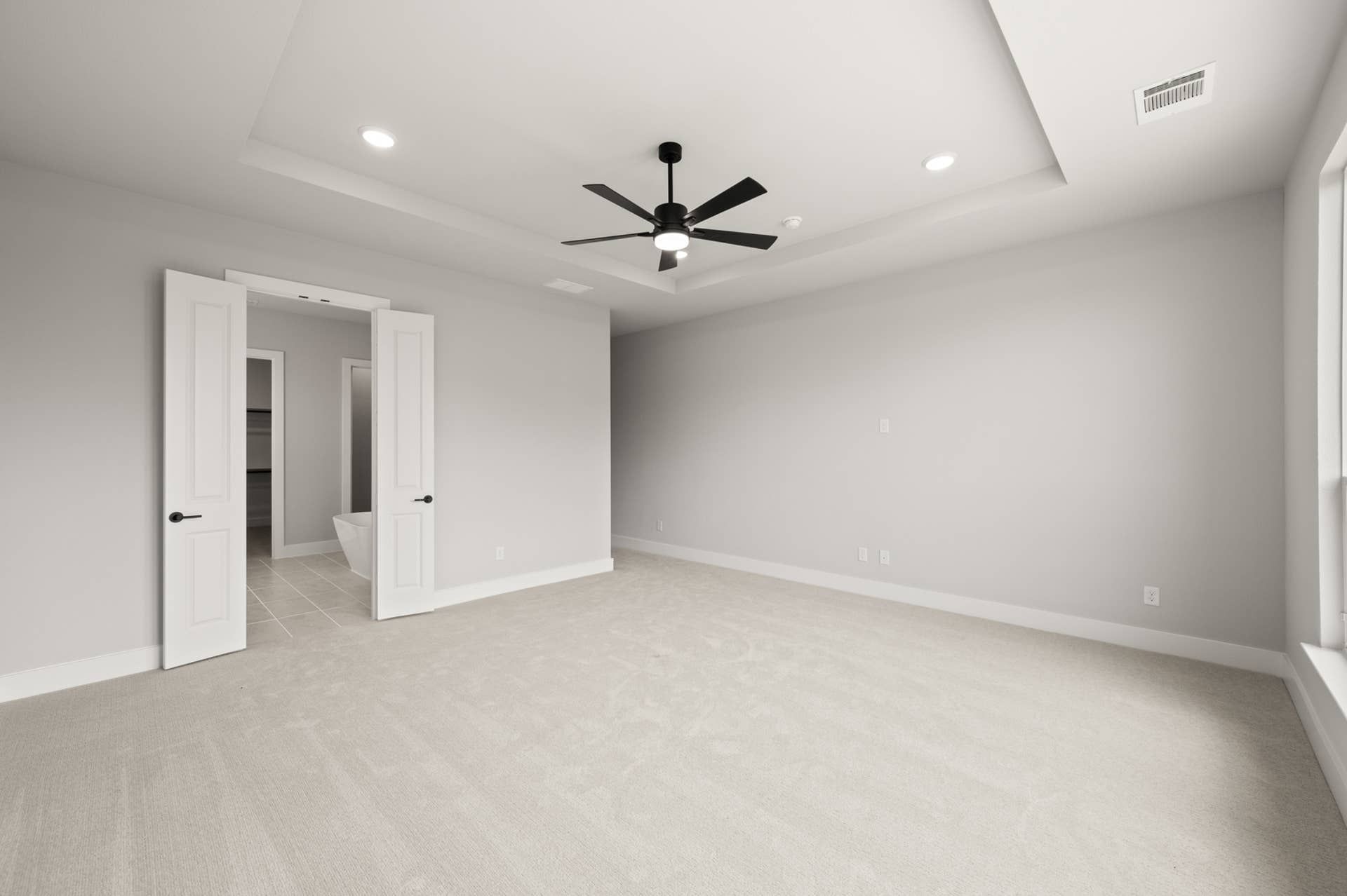 Spacious primary suite with neutral tones, ceiling fan, and double-door bathroom entry.