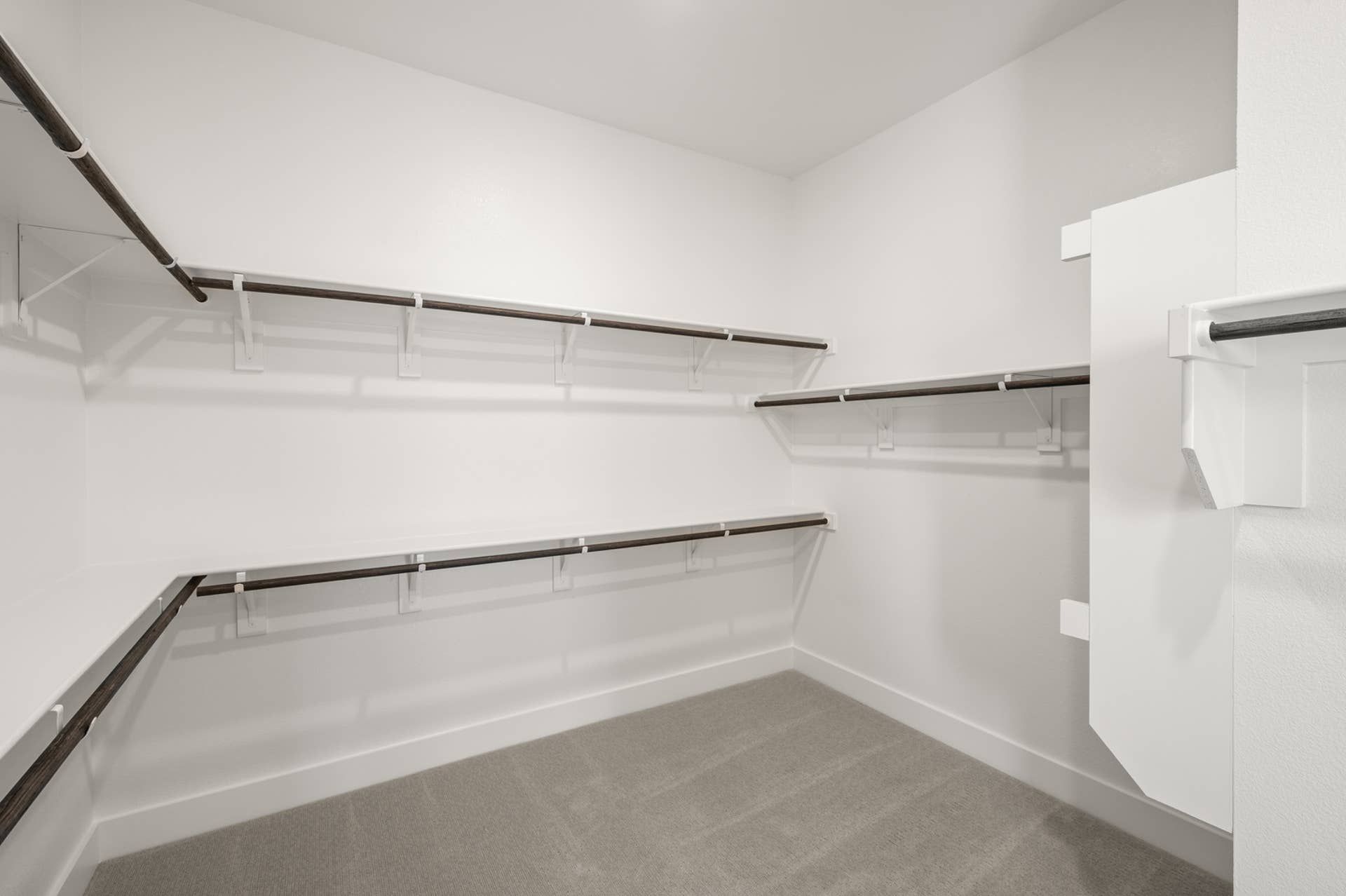Spacious walk-in closet with multiple hanging rods and white walls.