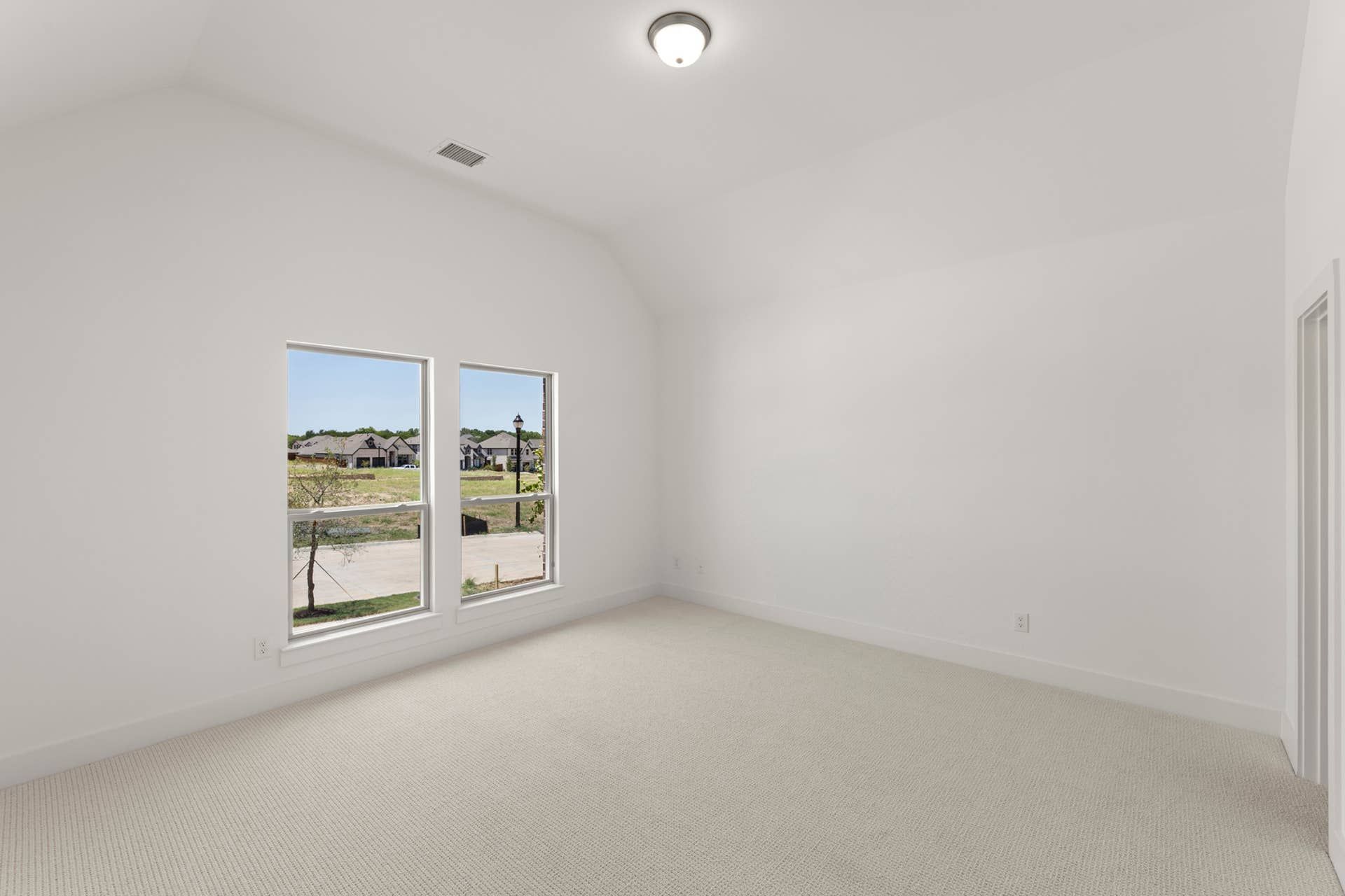 Spacious bedroom with large windows and neutral carpet flooring.