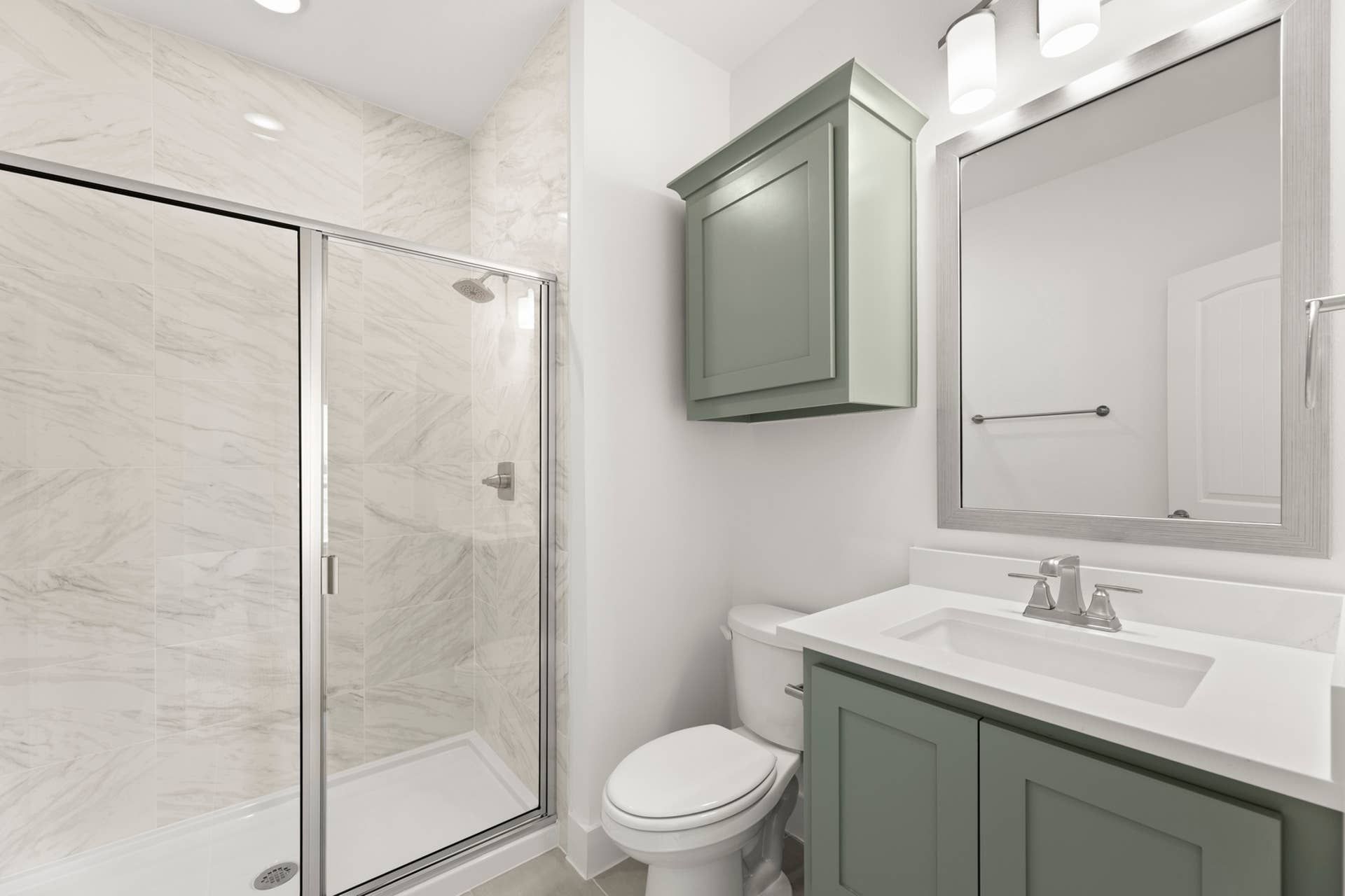 Modern bathroom with glass shower, green cabinetry, and large mirror.