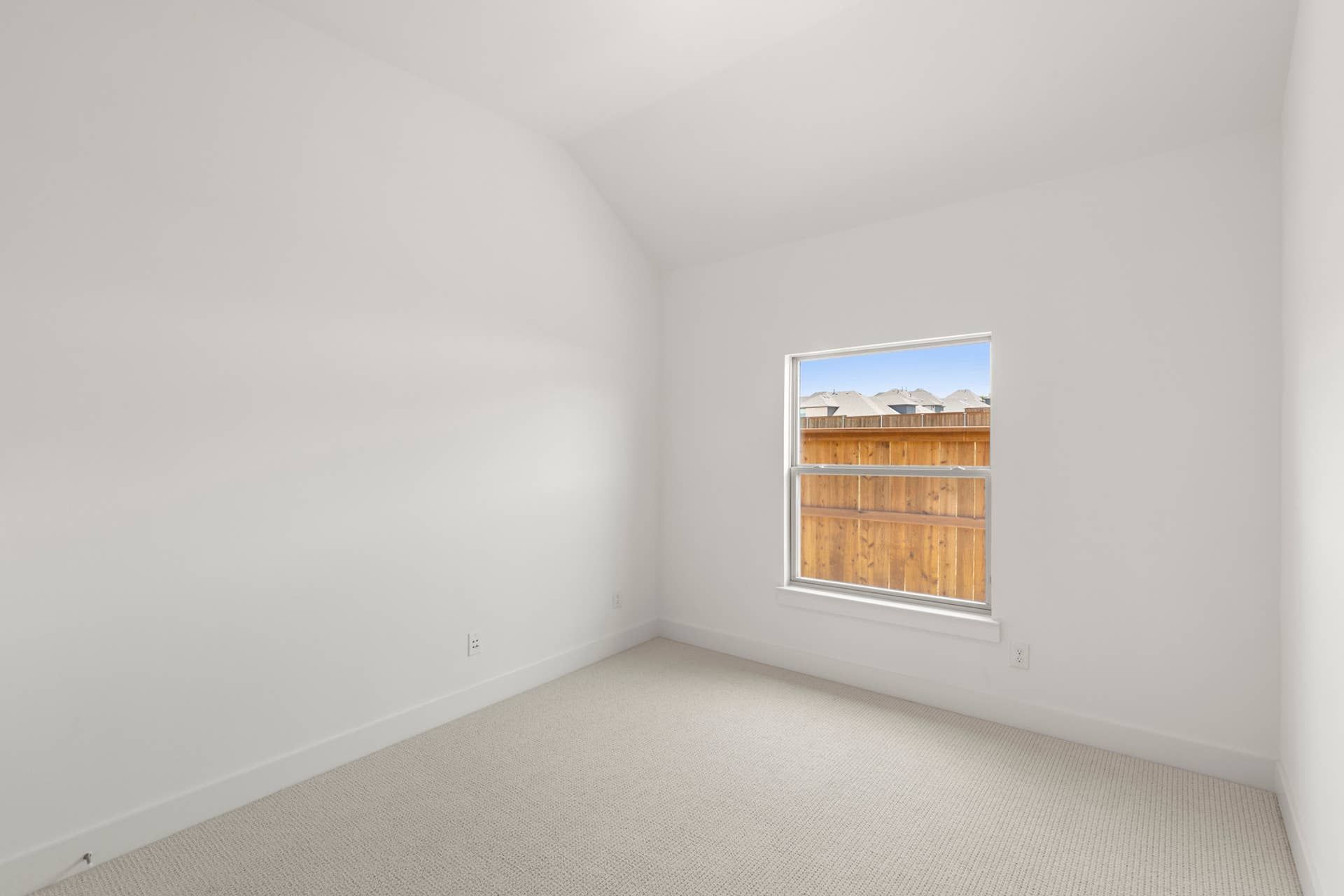 Minimalist bedroom with neutral carpeting and a single window view of wooden fence.