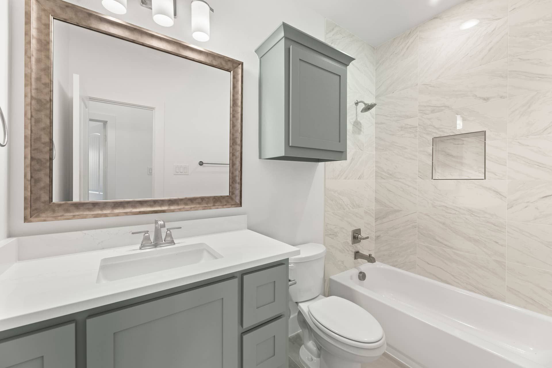 Modern bathroom with gray cabinetry, large mirror, and marble-tiled shower.