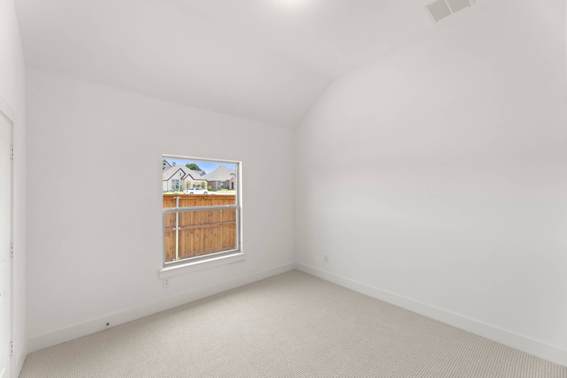 Empty bedroom with white walls and window overlooking wooden fence.