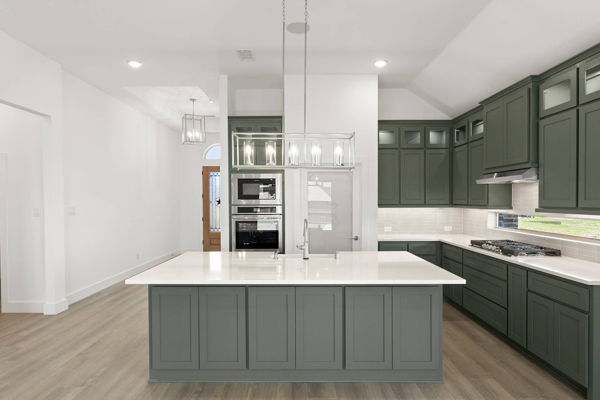 Modern kitchen with green cabinets, island, and stainless steel appliances.